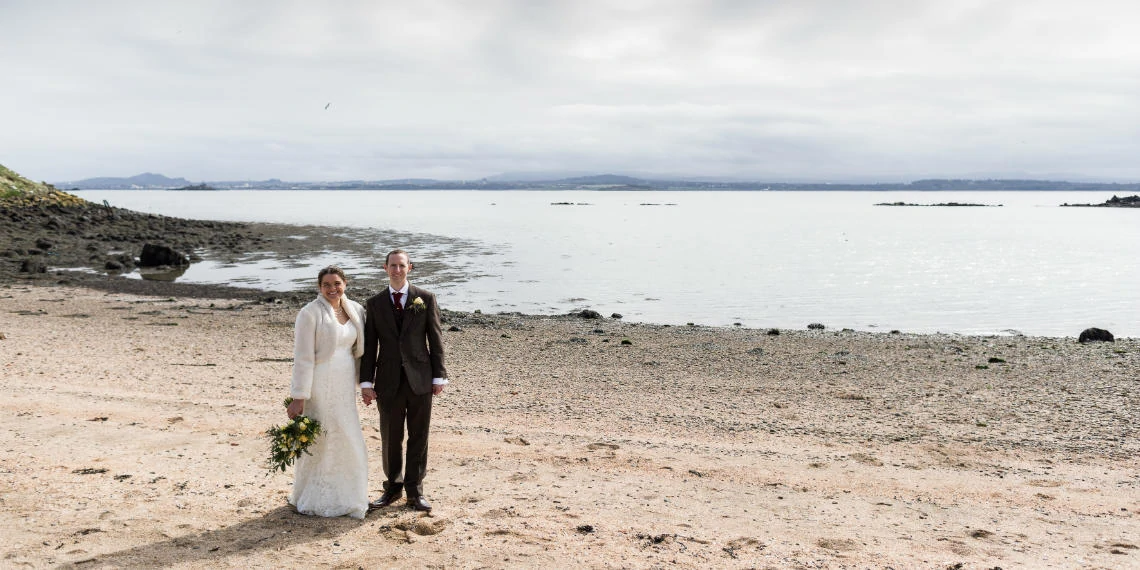 newlyweds on the beach with Edinburgh in the background across the Firth of Forth