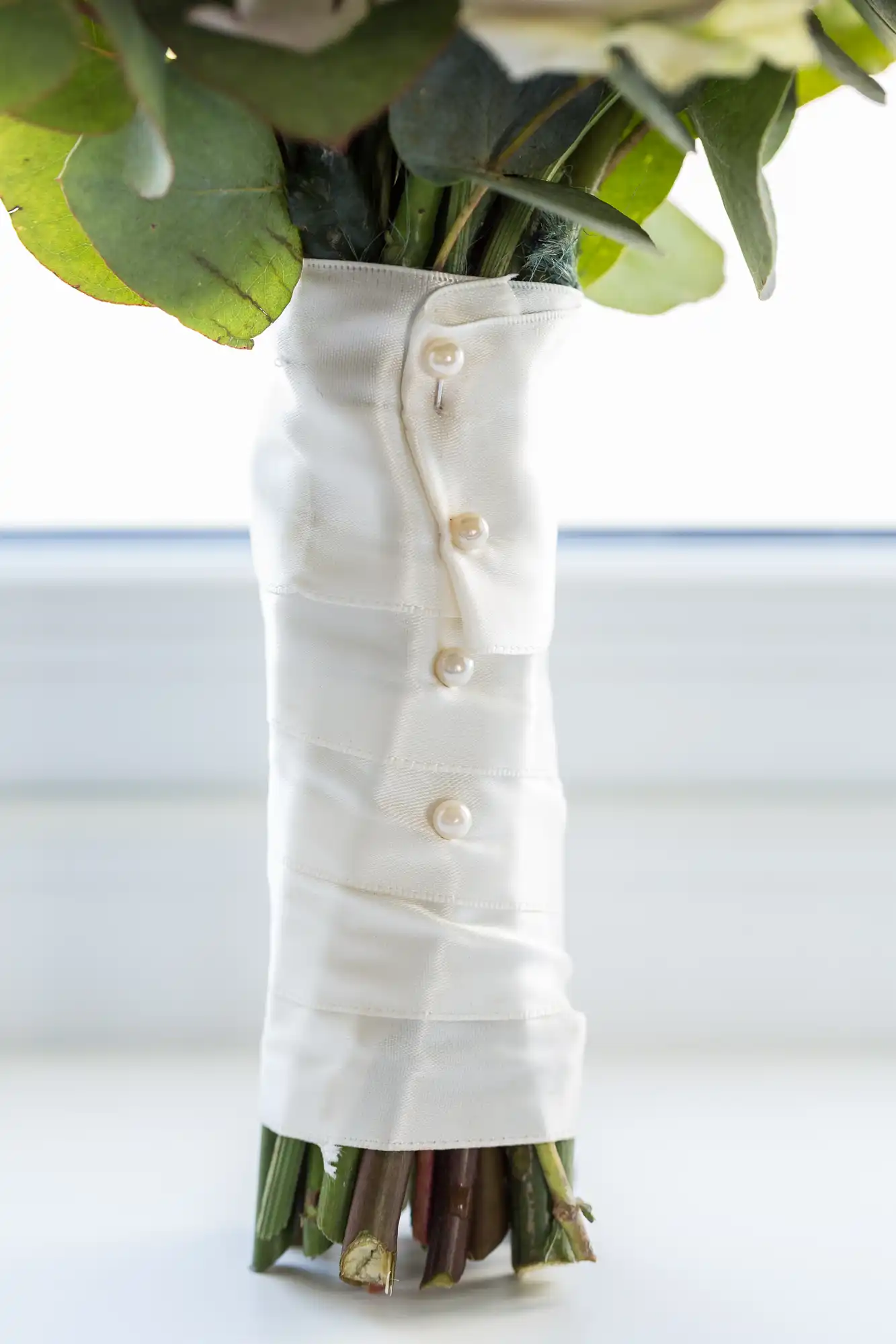 A bouquet of flowers wrapped in white fabric secured with buttons, placed against a bright background.