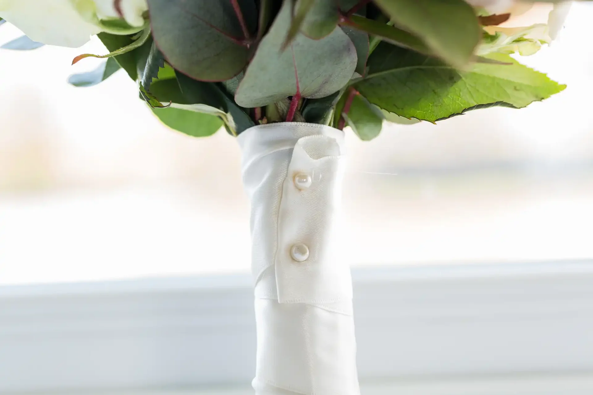 Bouquet of flowers with stems wrapped in a white fabric featuring button details, set against a softly blurred background.