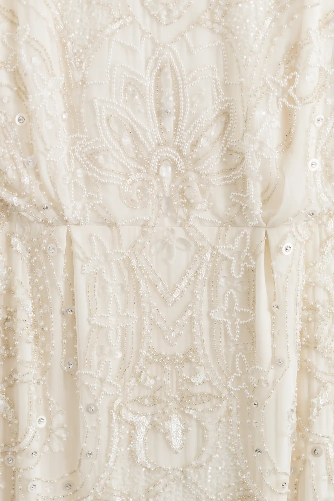 Close-up of an intricate, beaded white dress featuring symmetrical floral embellishments.