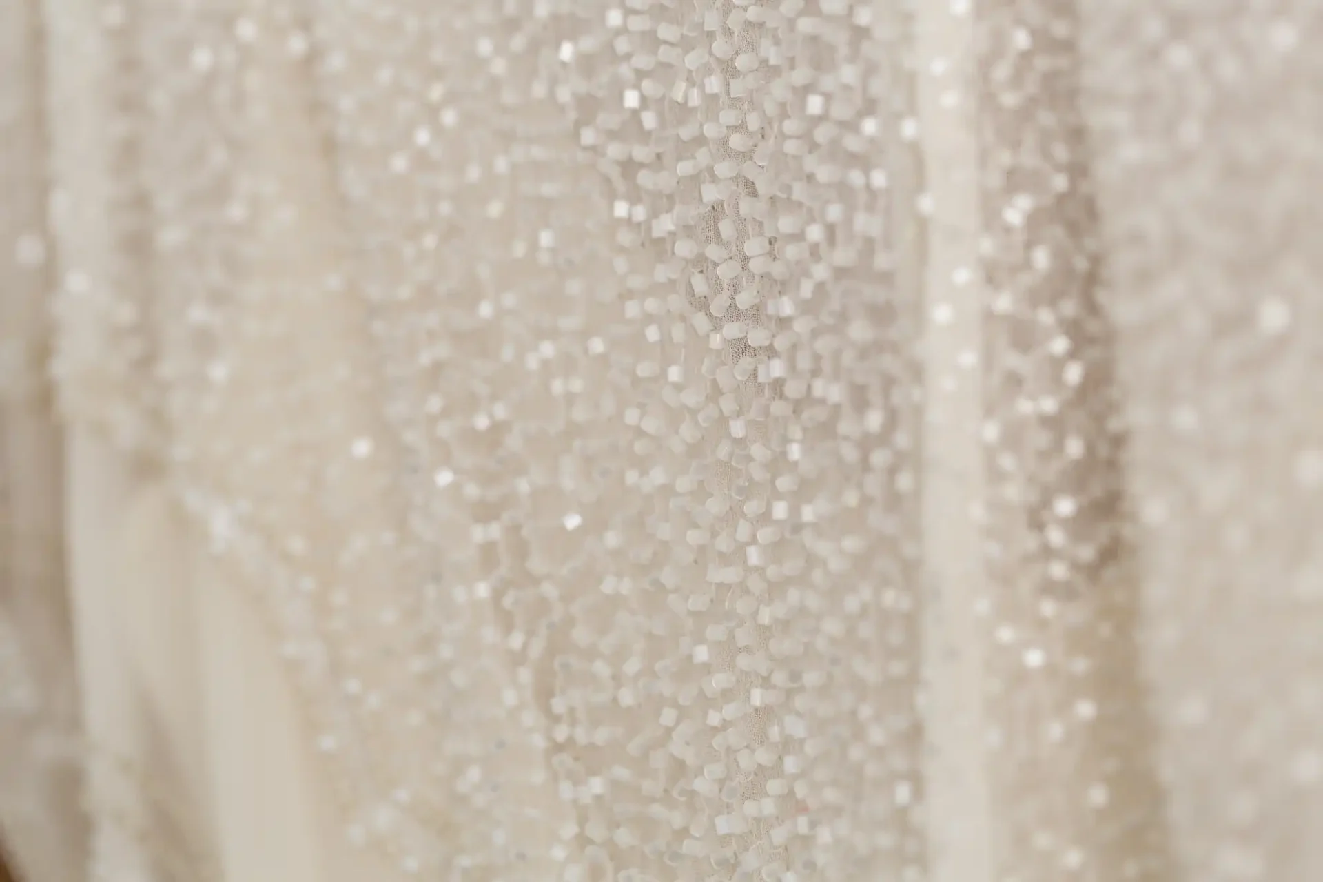 Close-up of a beige fabric adorned with numerous small, shiny beads creating a textured, glittery surface.