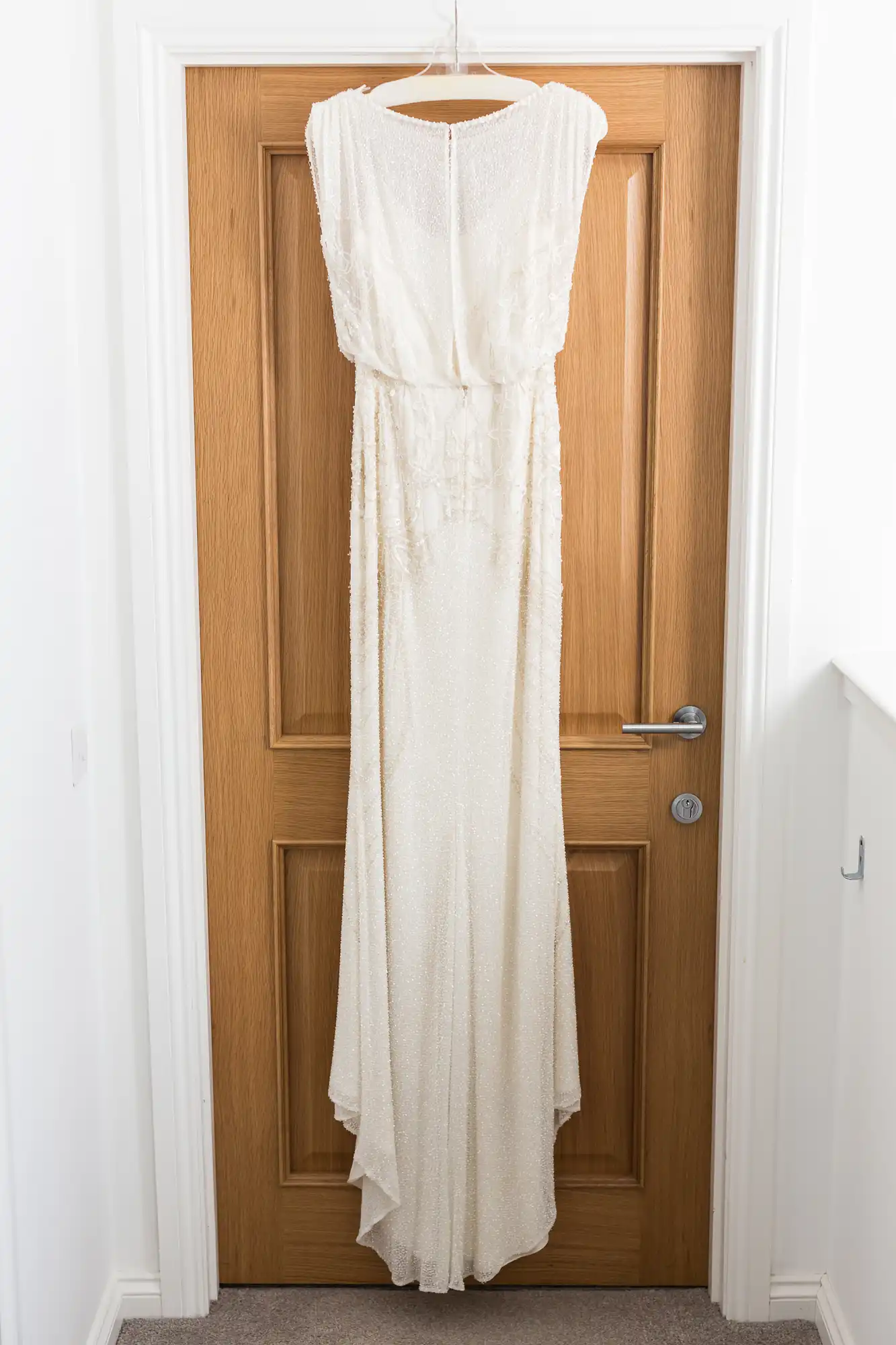 A long, white, beaded wedding dress hanging on a wooden door.