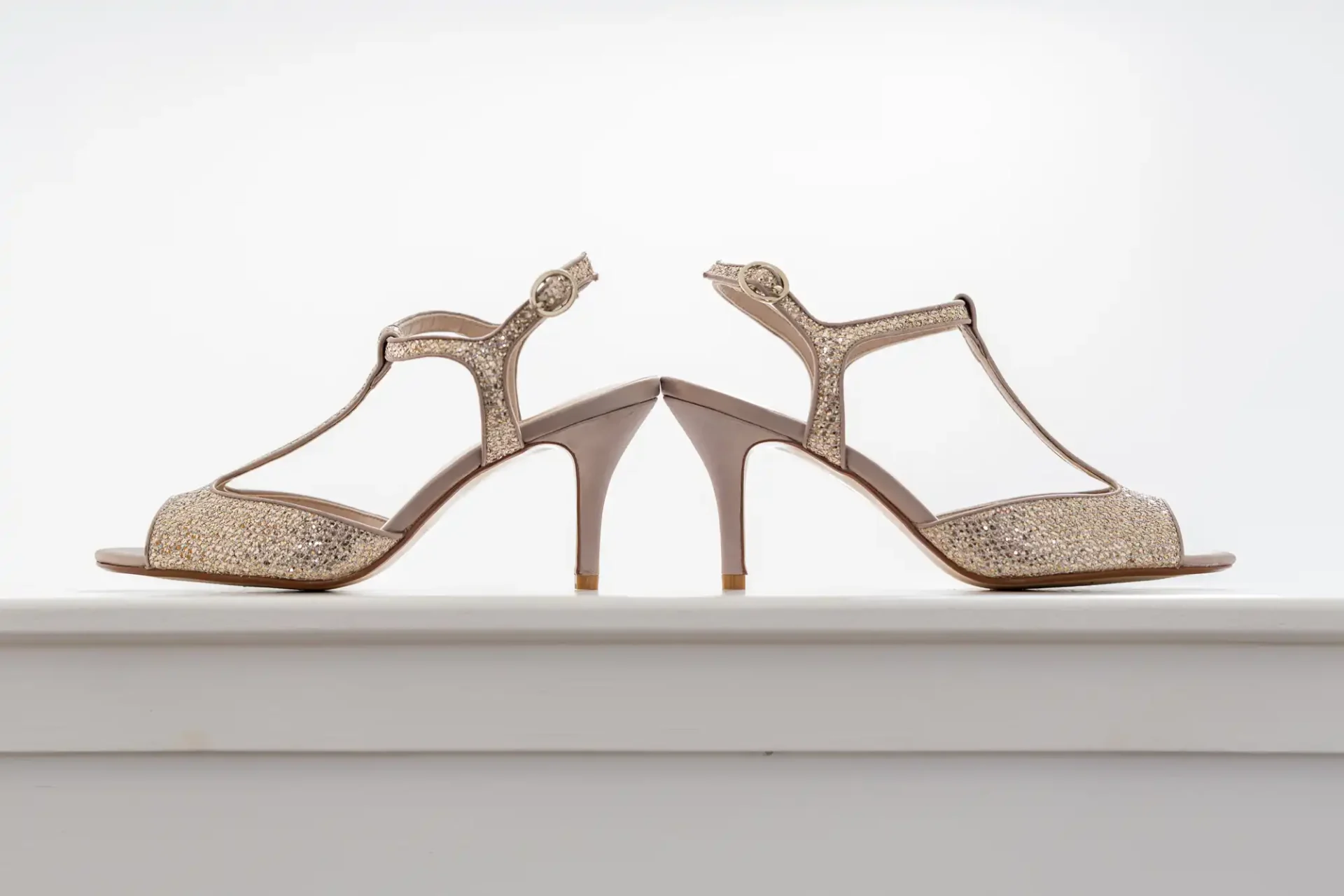 A pair of elegant high-heeled sandals with glittery embellishments on a white background.