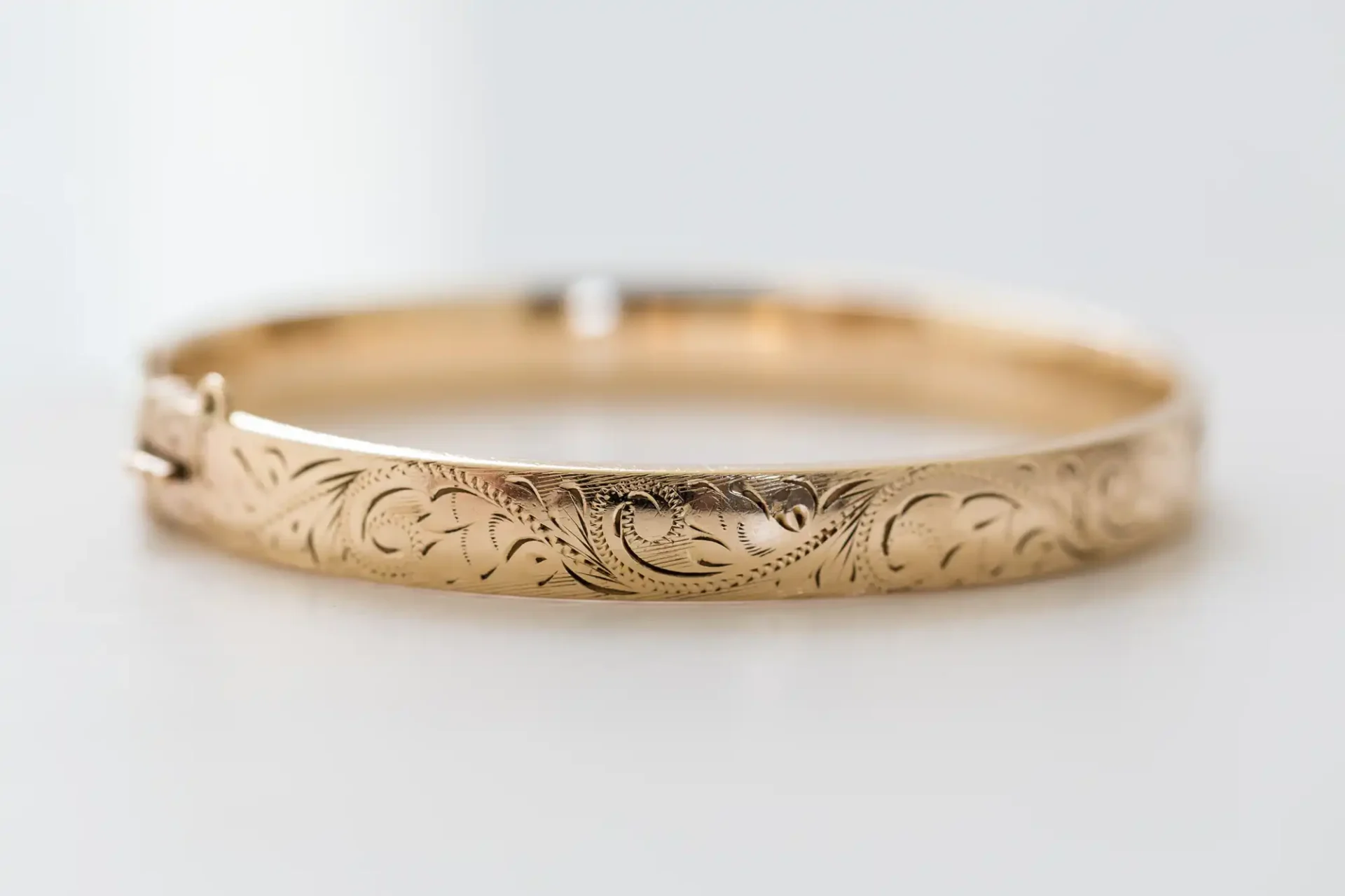Gold bracelet with intricate floral engraving, displayed against a soft white background.