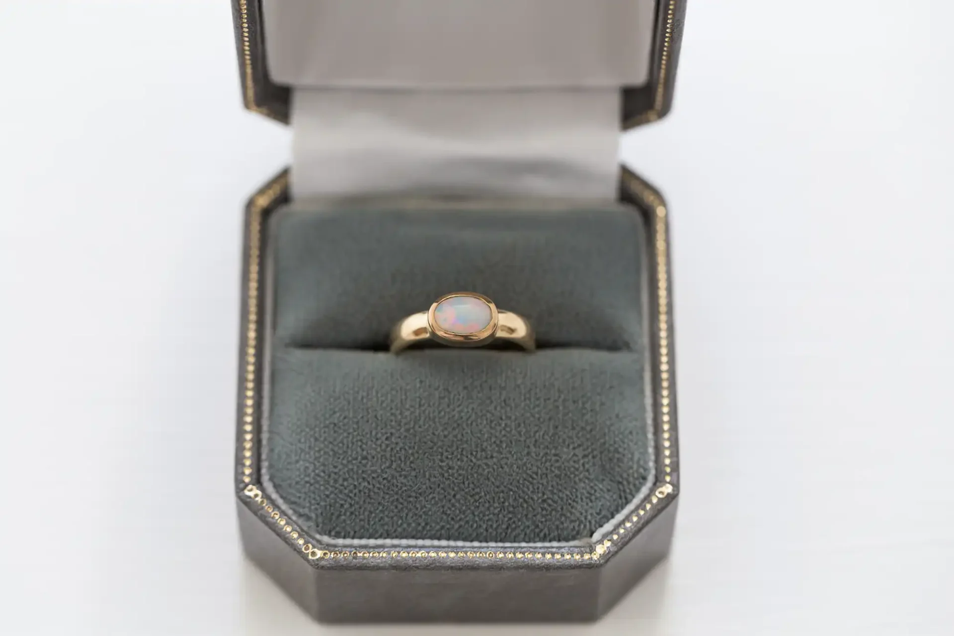 Gold ring with an opal stone set in a gray padded jewelry box on a white background.