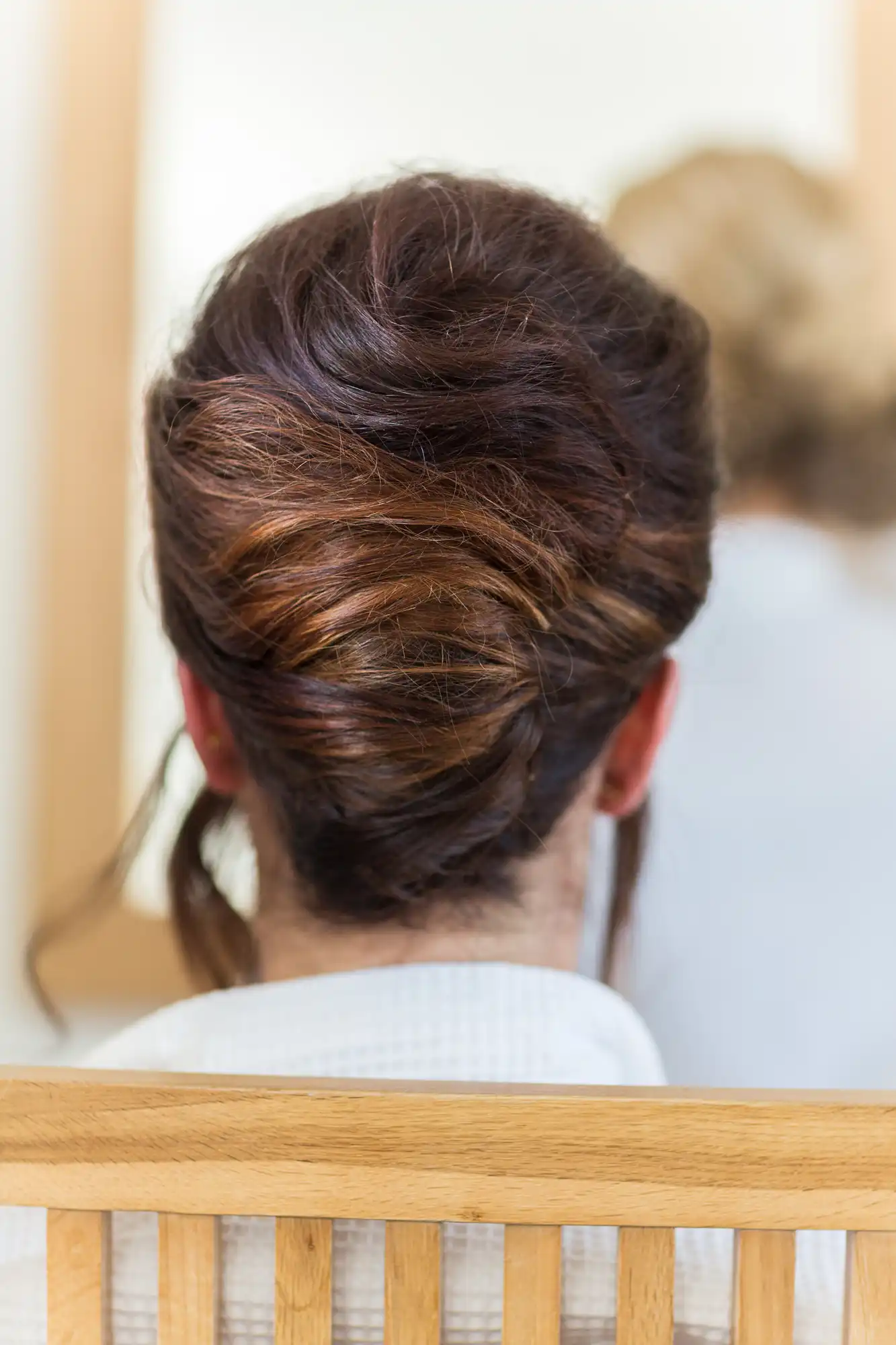 Close-up of a woman's head from behind, showing her brown hair styled in an elegant updo, with visible hairpins.