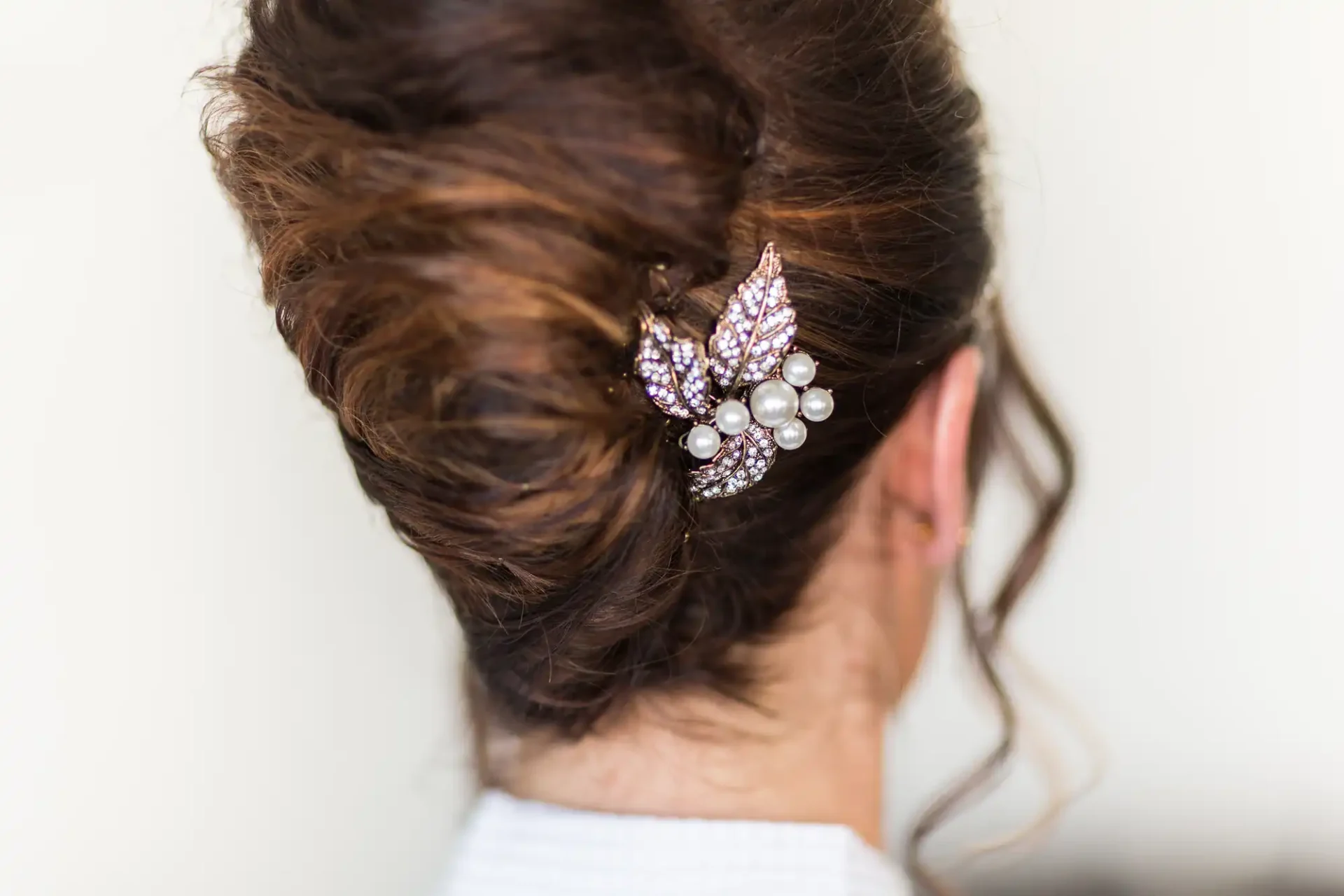 An elegant updo hairstyle adorned with a decorative hairpin featuring pearls and glittering crystals.