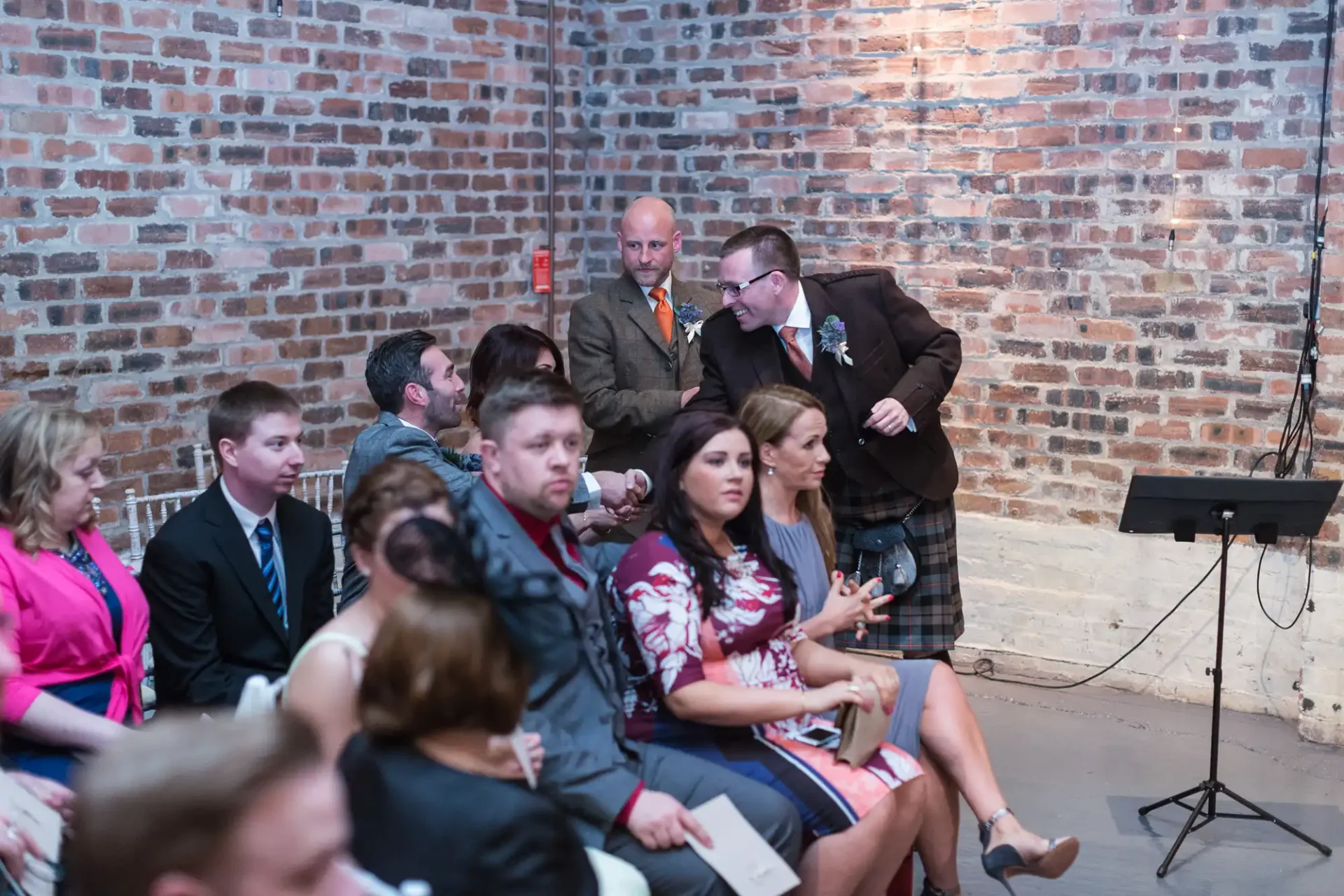 A group of people sitting on chairs in a room with brick walls, attentively watching a speaker not visible in the image.