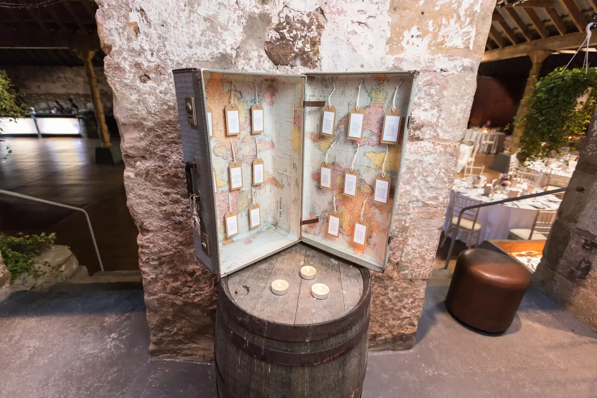 Vintage style open wooden cabinet with maps and pinned notes, displayed on a wooden barrel in a rustic room setting.