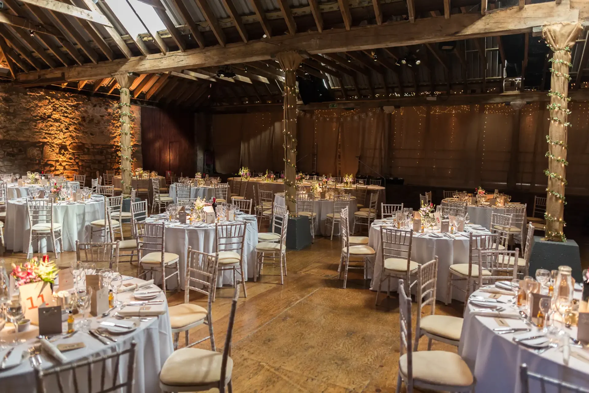 Elegant barn wedding venue with decorated tables, string lights, and exposed wooden beams.