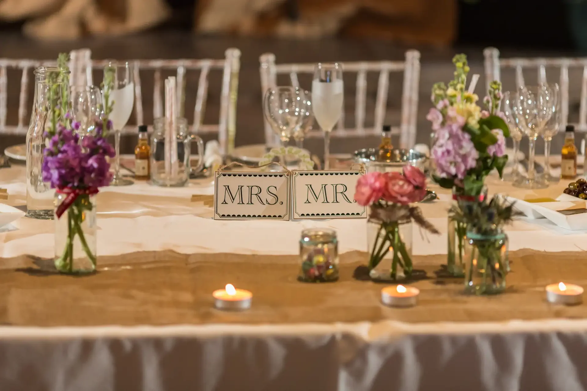 Elegant wedding table setting with "mrs." and "mr." signs, floral arrangements, candles, and multiple glasses.