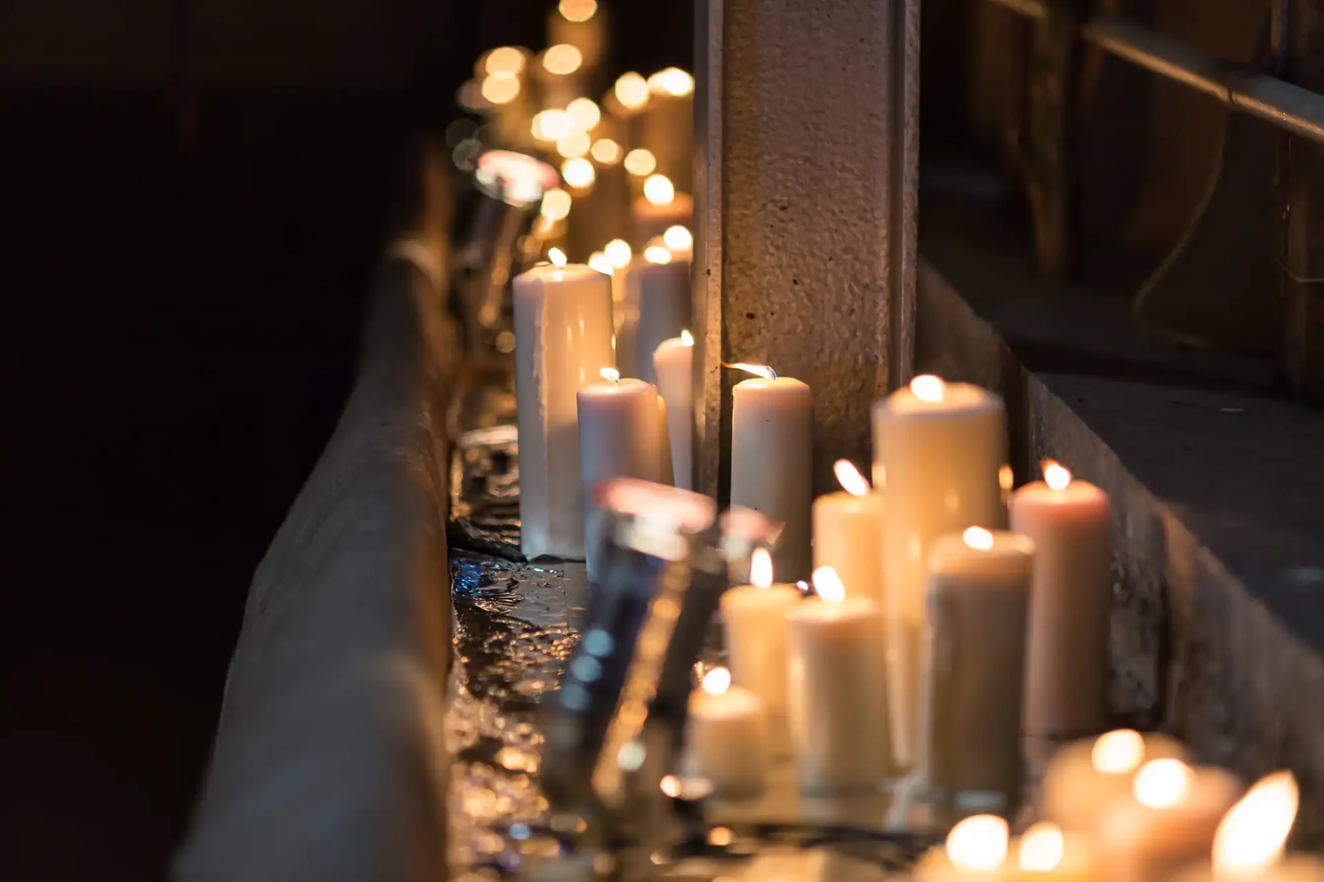 Candles with flickering flames lined up along a narrow ledge, casting a warm glow on the surrounding area.