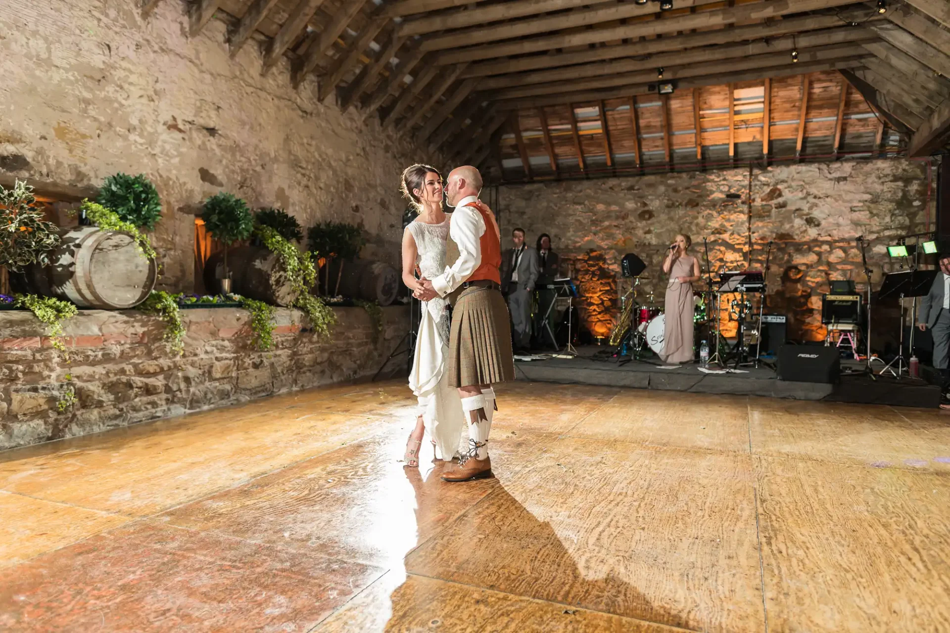 A bride and groom share a dance in a rustic barn venue with a band playing in the background.