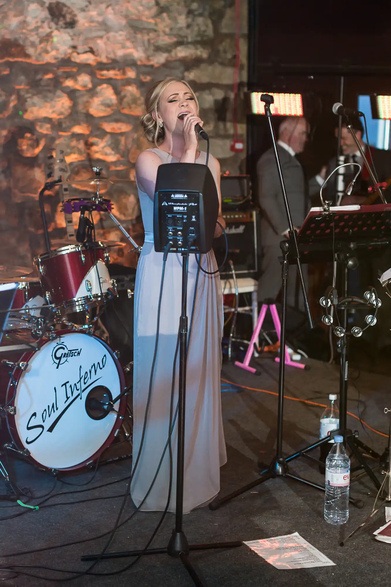 A female singer performing at a live event with a band named soul inferno in the background, using a microphone and a music stand.