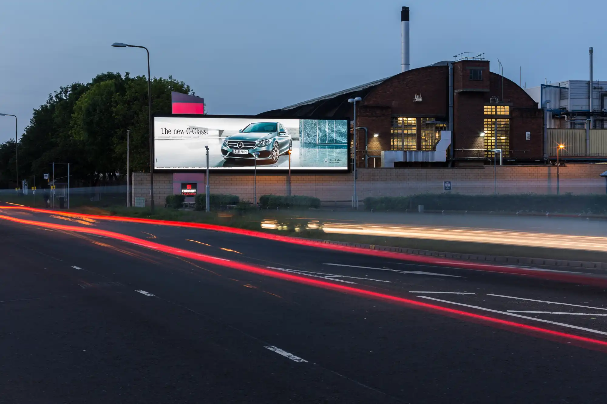 A time-lapse photo of a road at dusk shows red and white light trails from moving vehicles. A large billboard displaying a car advertisement is visible in the background.