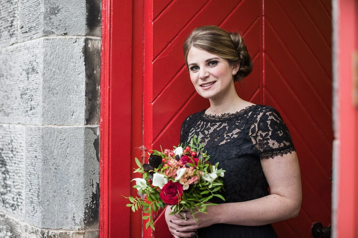 bridesmaid holding a bouquet in front of a red door at Liberton Kirk