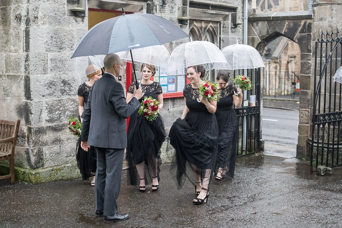 bridesmaids under umbrellas as they wait for the arrival of the bride at Liberton Kirk