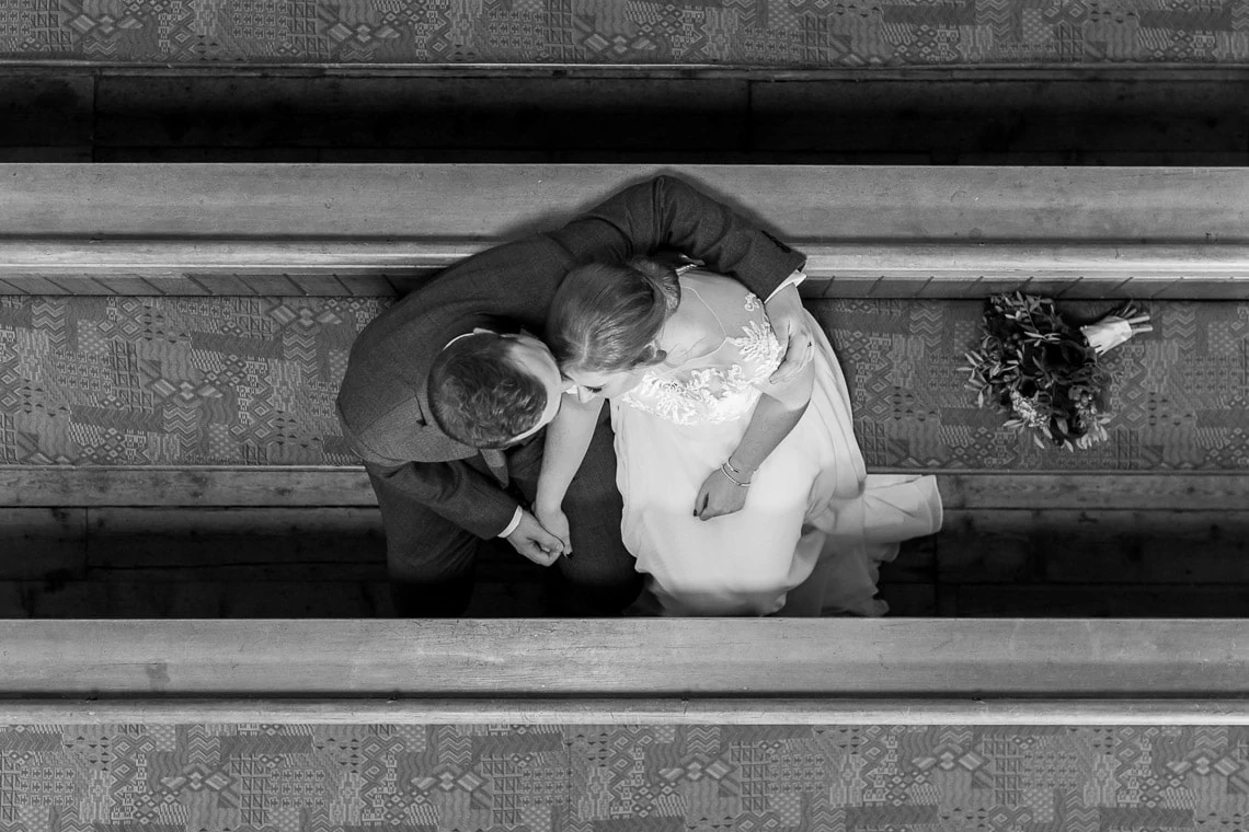 newlyweds embrace sitting on a pew viewed from above