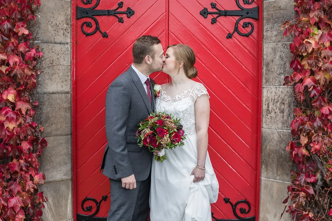 newlyweds kiss in front of the red doors at Liberton Kirk
