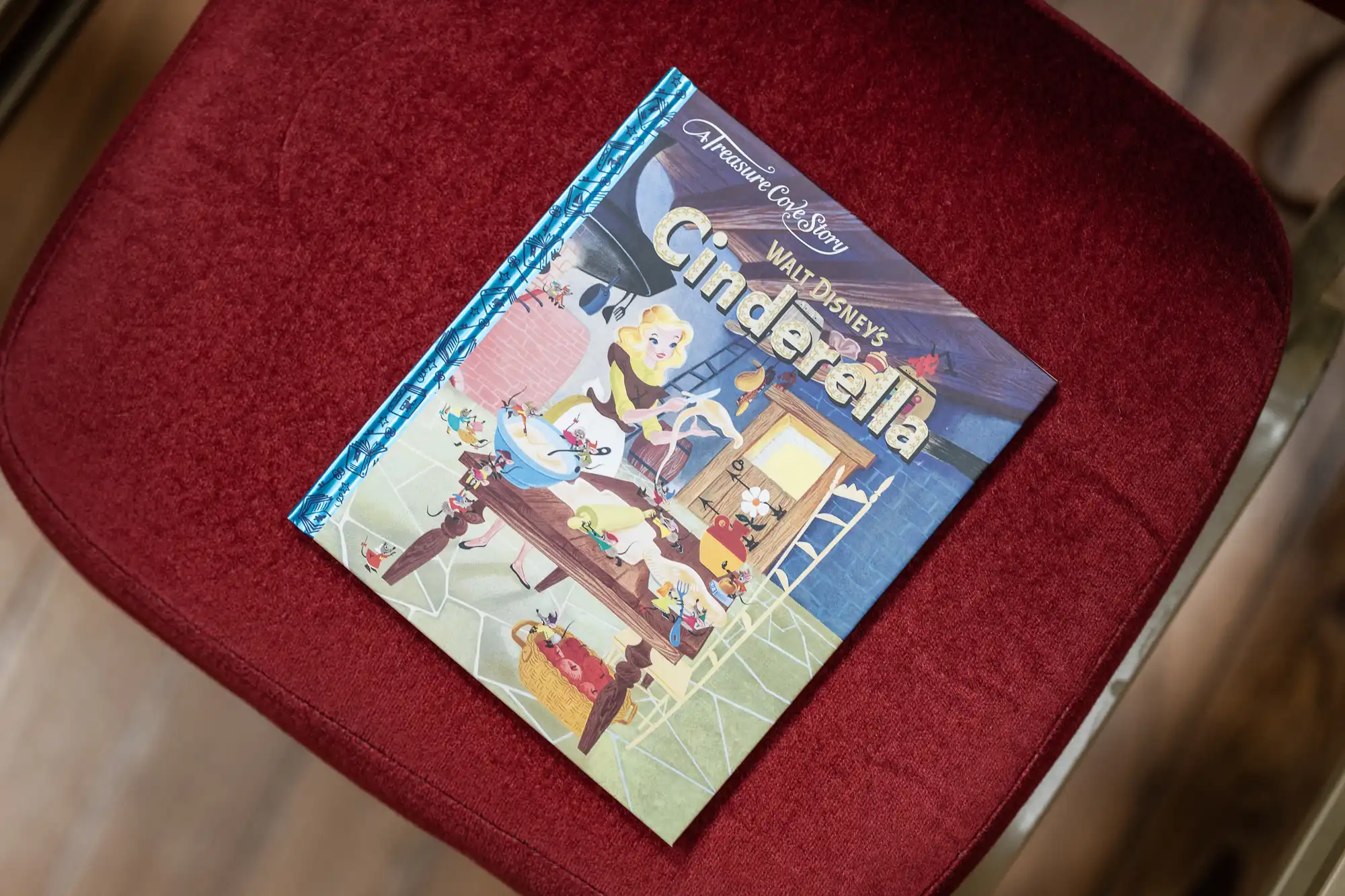 A children's book titled "Walt Disney's Cinderella" with colorful illustrations is placed on a red cushioned surface.