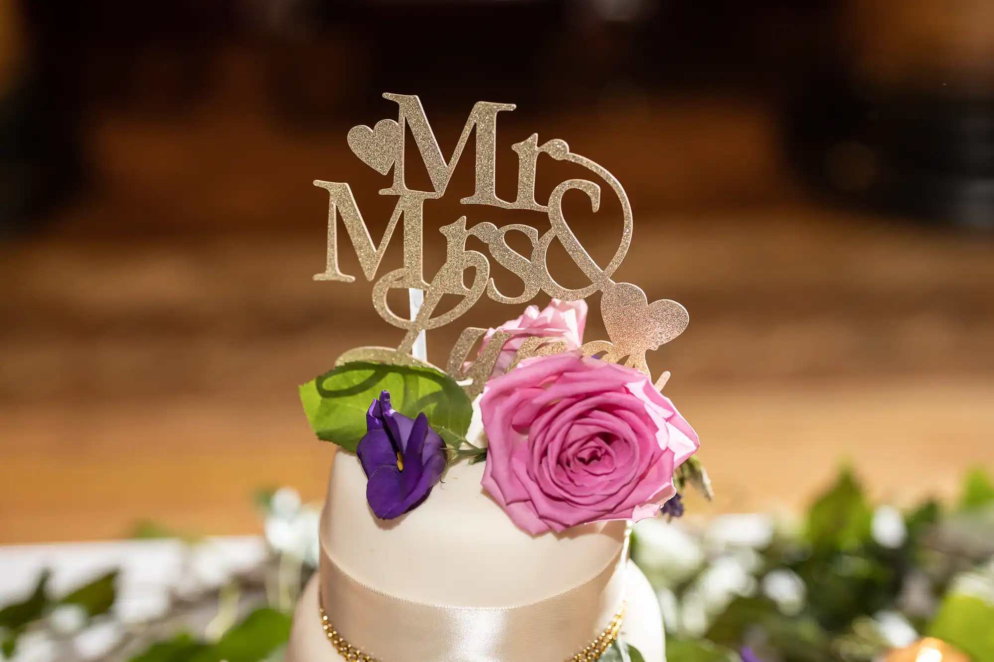 Close-up of a wedding cake topped with a "Mr & Mrs" decoration and adorned with pink and purple flowers.