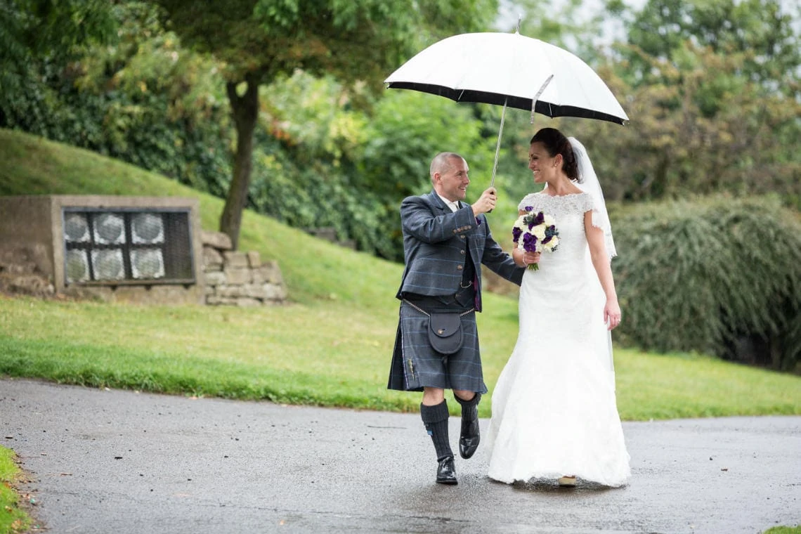 newlyweds on Calton Hill walking under an umbrella