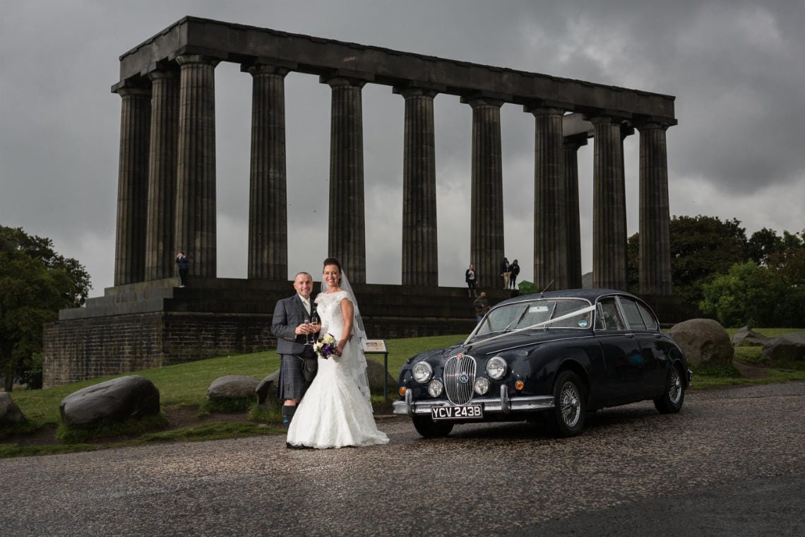 newlyweds on Calton Hill next to a classic Mark 2 Jaguar with the National Monument in the background