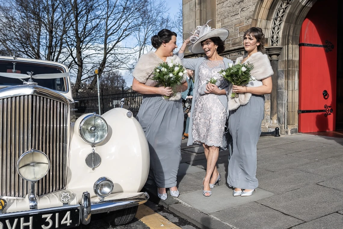 bridesmaids and mother of the bride waiting at the entrance next to a classic wedding car