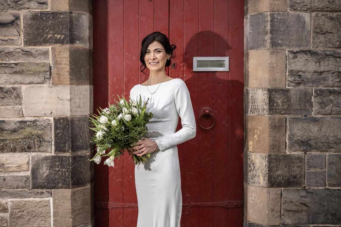 bride holding her bouquet in front of a red door