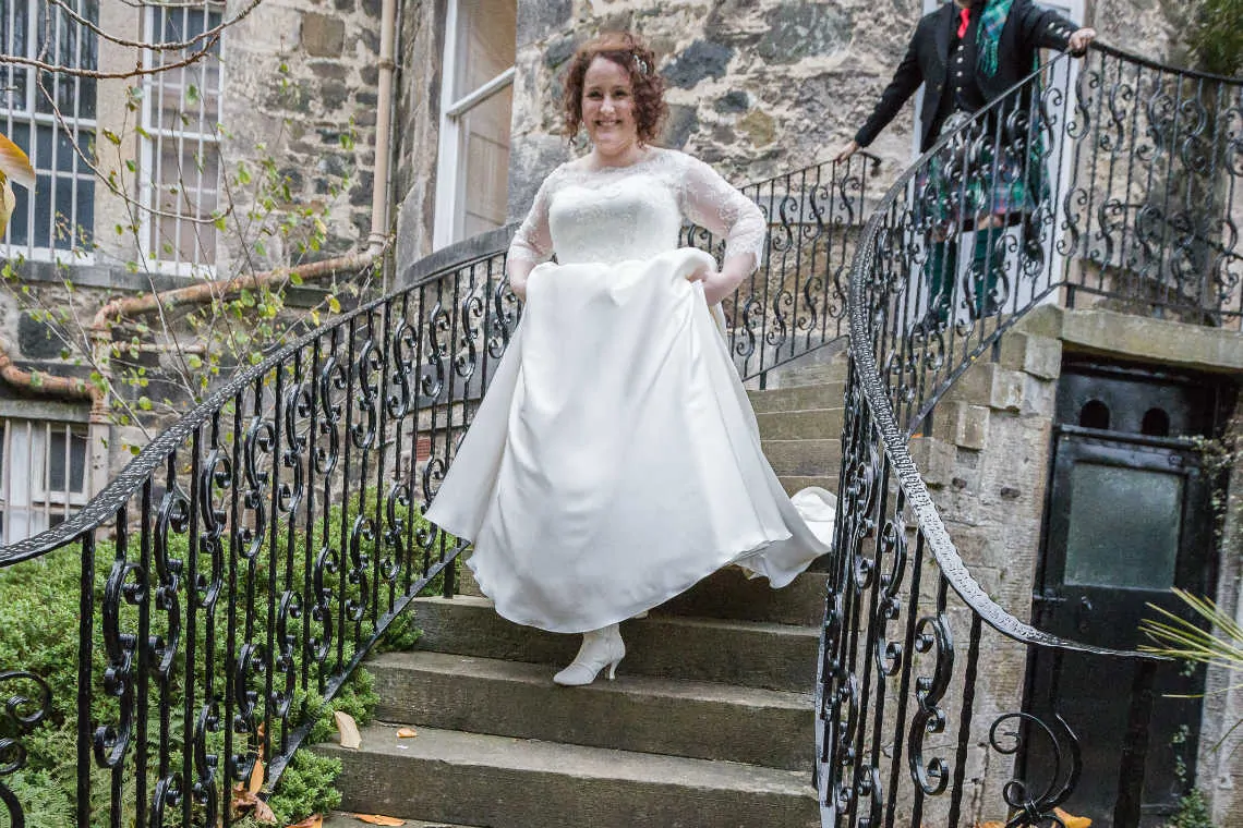 Bride outside walking down staircase holding up wedding dress