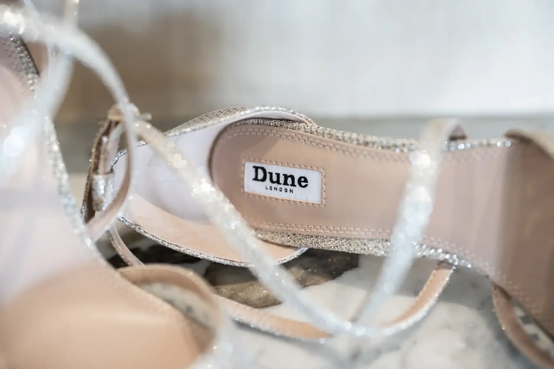 Close-up of silver glittery high-heeled sandals with a visible "Dune London" label inside.