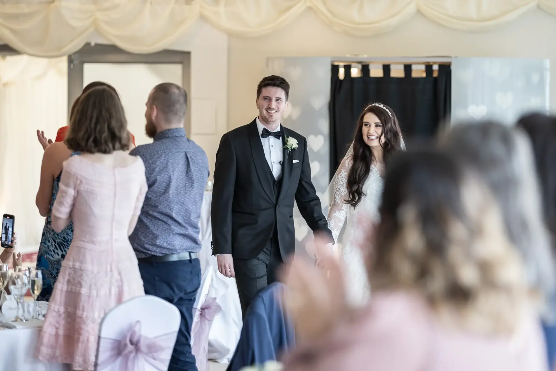 Bride and groom enter a reception hall as guests stand and clap.