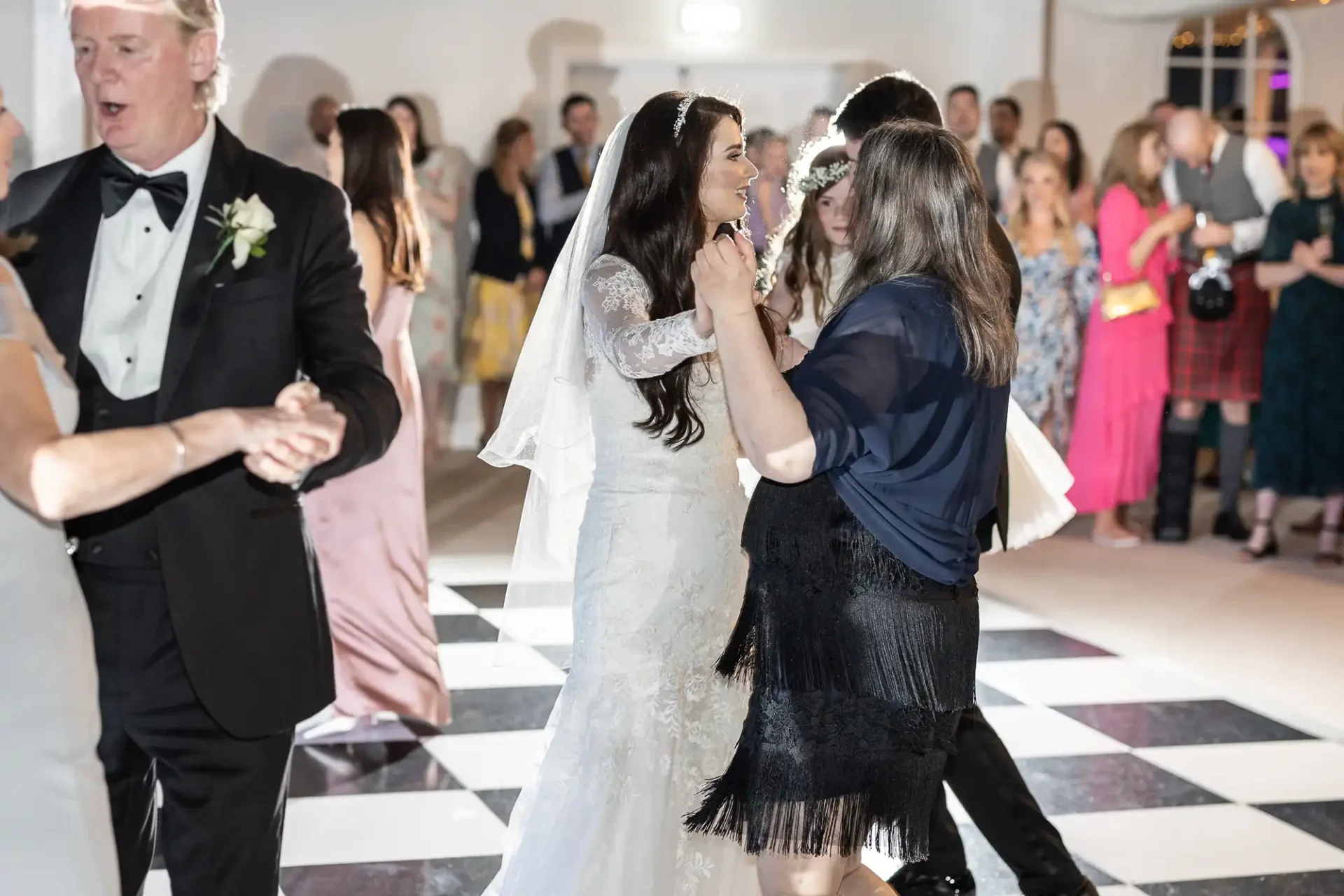 Bride dancing with guests on a black and white checkered dance floor at a wedding reception, surrounded by other attendees.