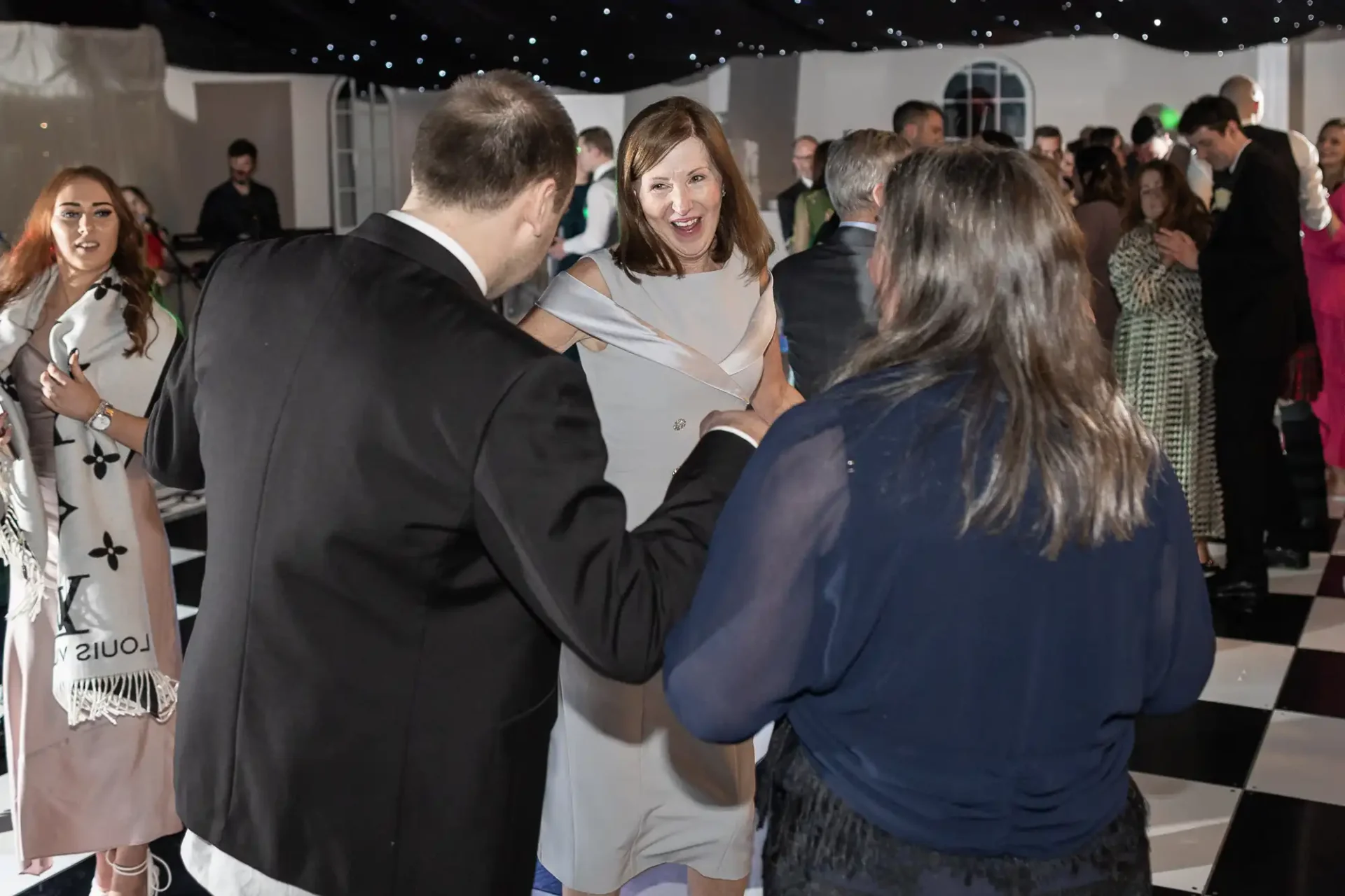 People dancing at an indoor event with a black and white checkered floor and starry ceiling decor.