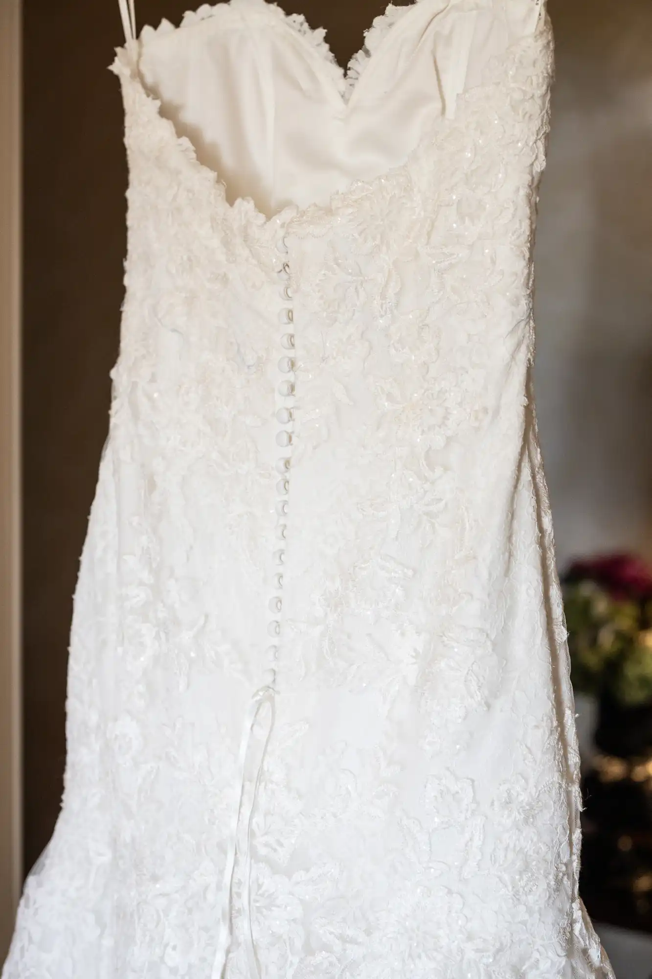 Strapless white lace wedding dress hanging, featuring a row of buttons down the back.