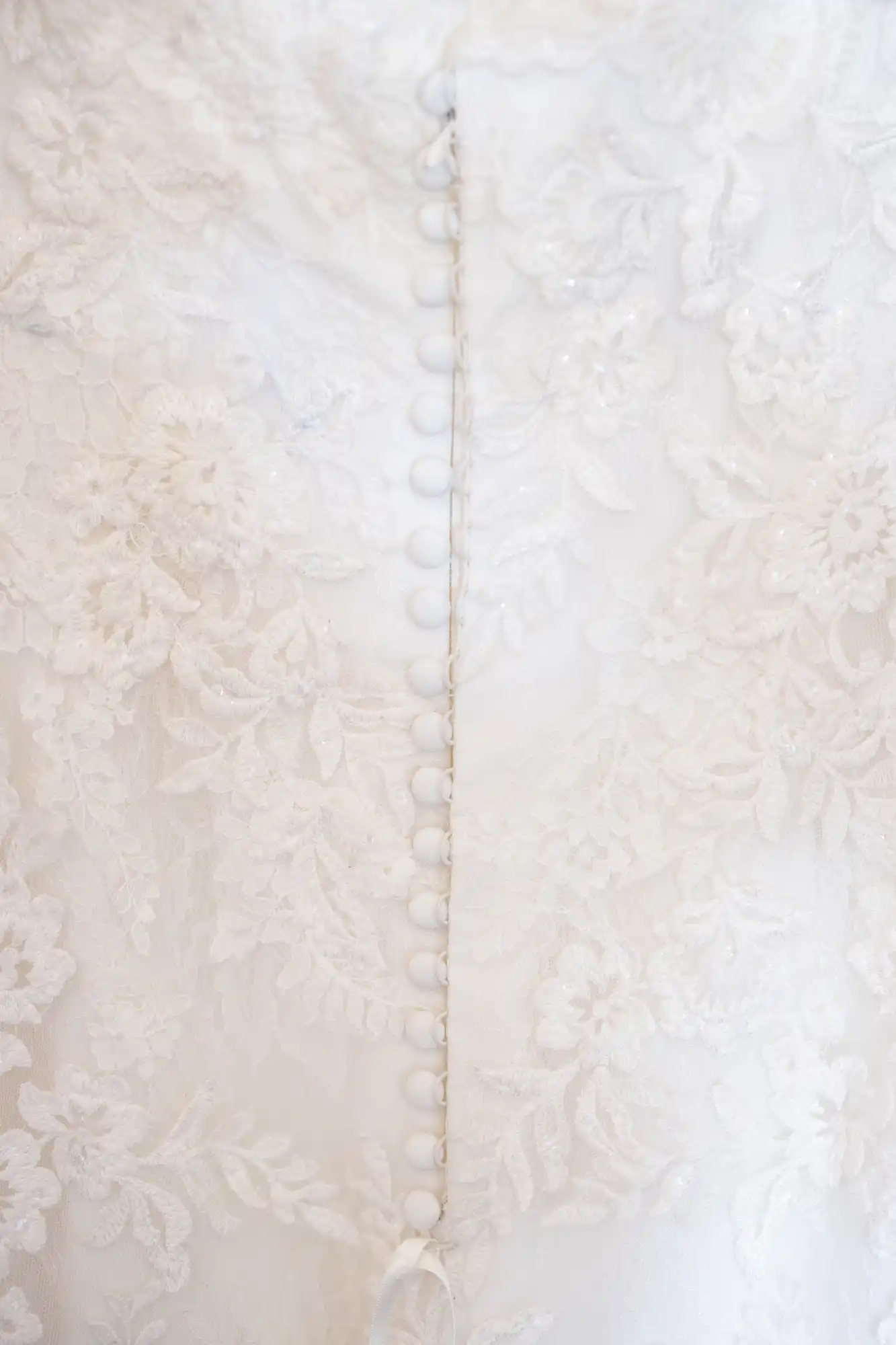 Close-up of the back of a white lace bridal gown with a row of small white buttons down the center.