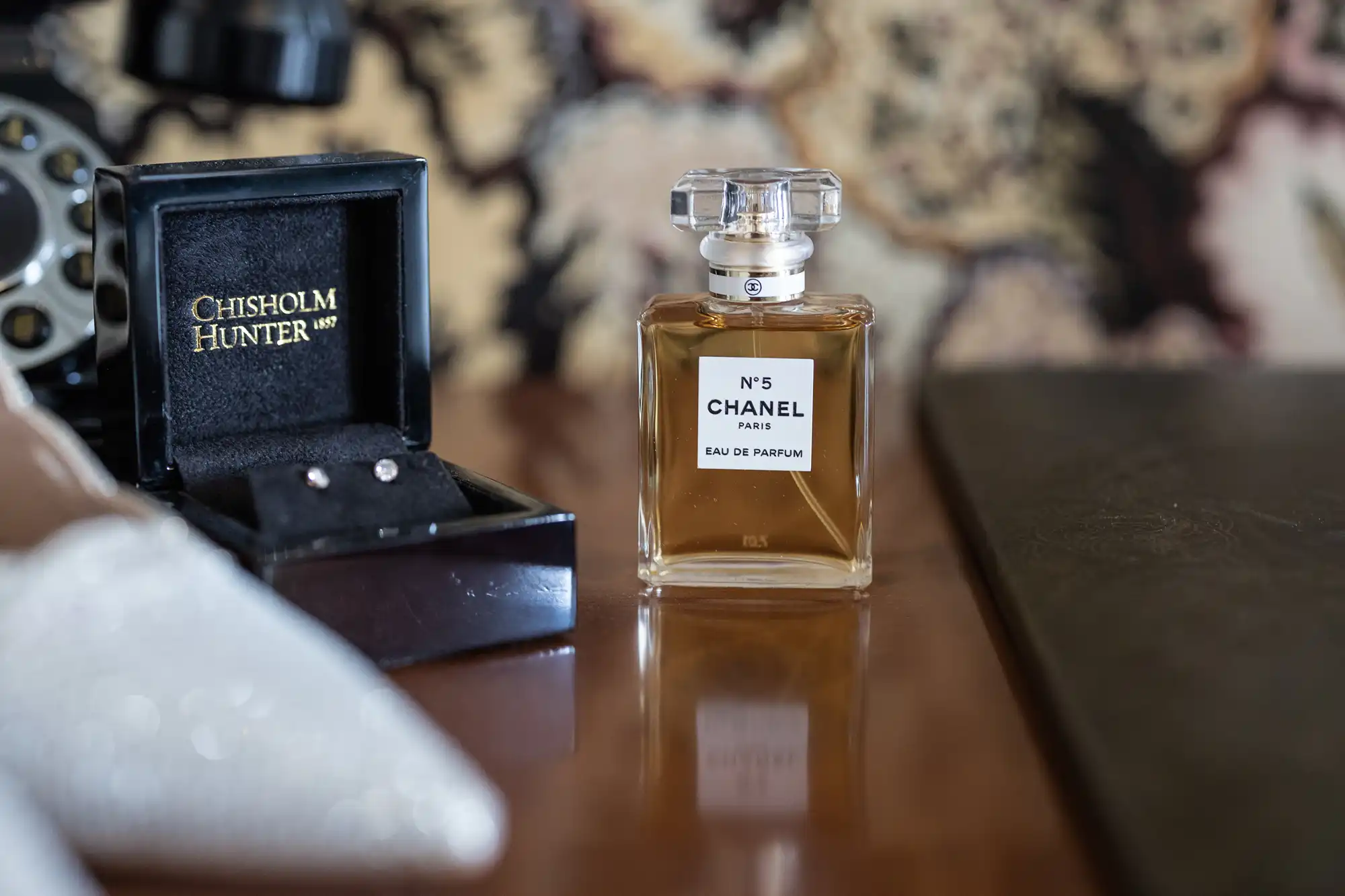 A bottle of Chanel No. 5 perfume on a table with a jewelry box and camera in the background.