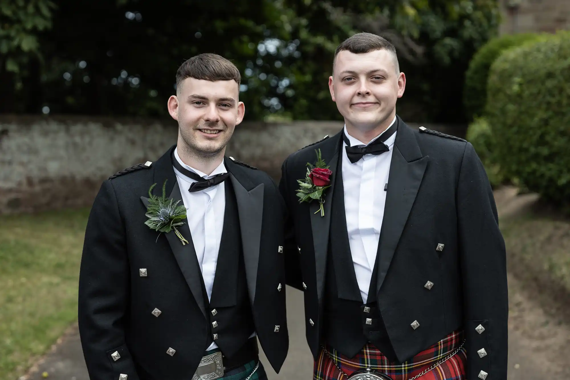 Two men in Scottish attire with kilts and jackets, smiling at a formal outdoor event.