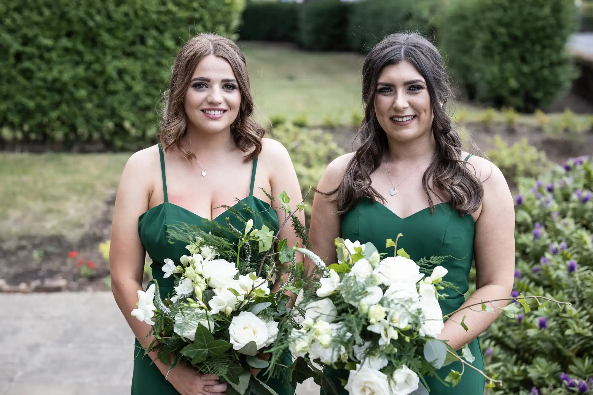 Two women in green dresses holding bouquets, standing in a garden.