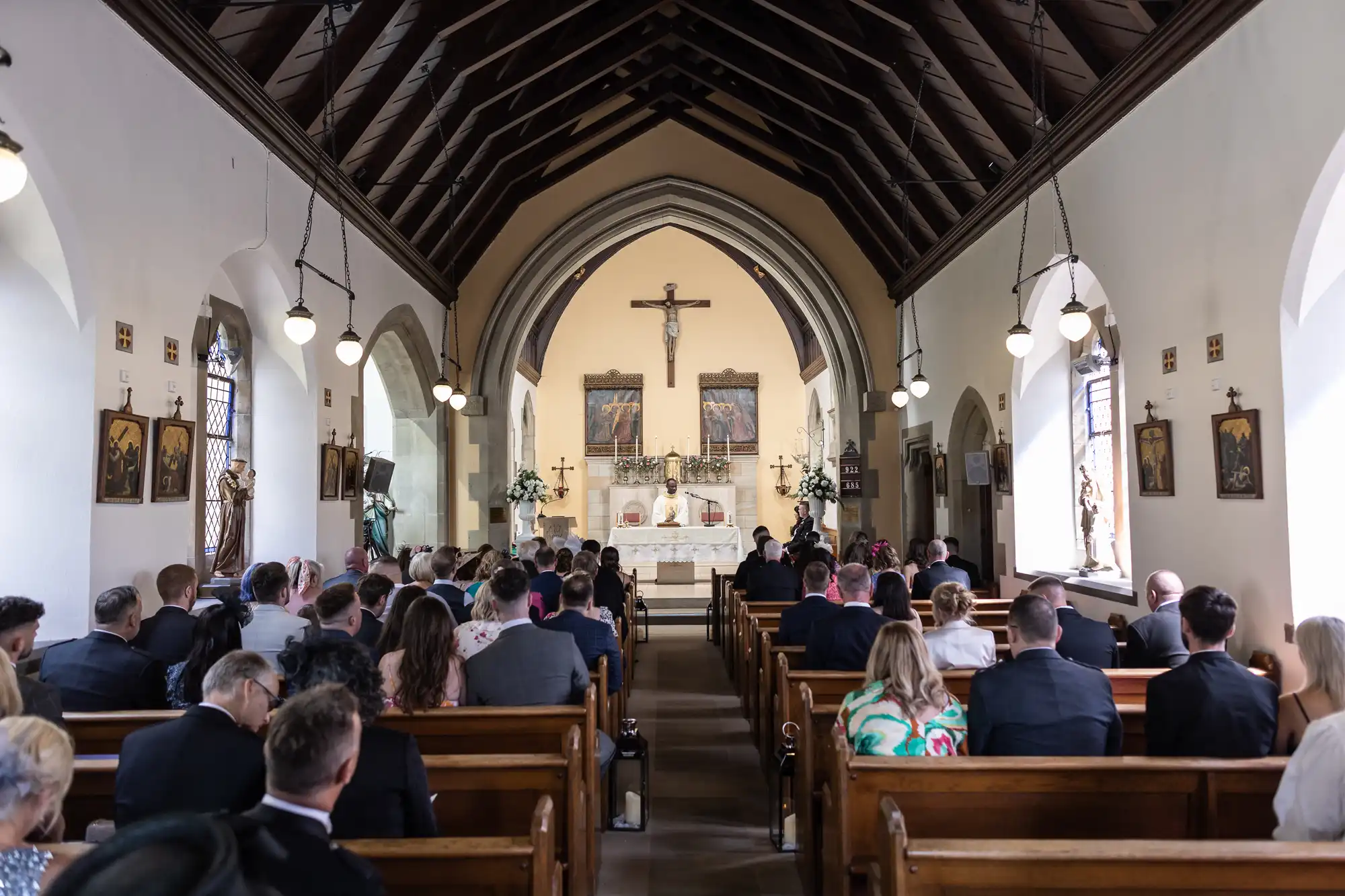 A wedding ceremony inside a church with guests seated in pews and a couple at the altar under a wooden arched ceiling.
