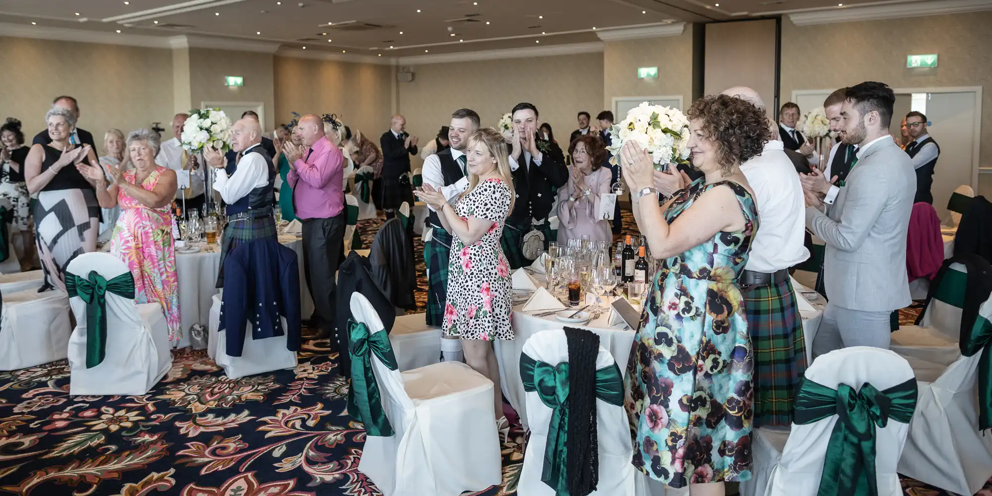 Guests standing and applauding at a wedding reception inside an elegantly decorated room.
