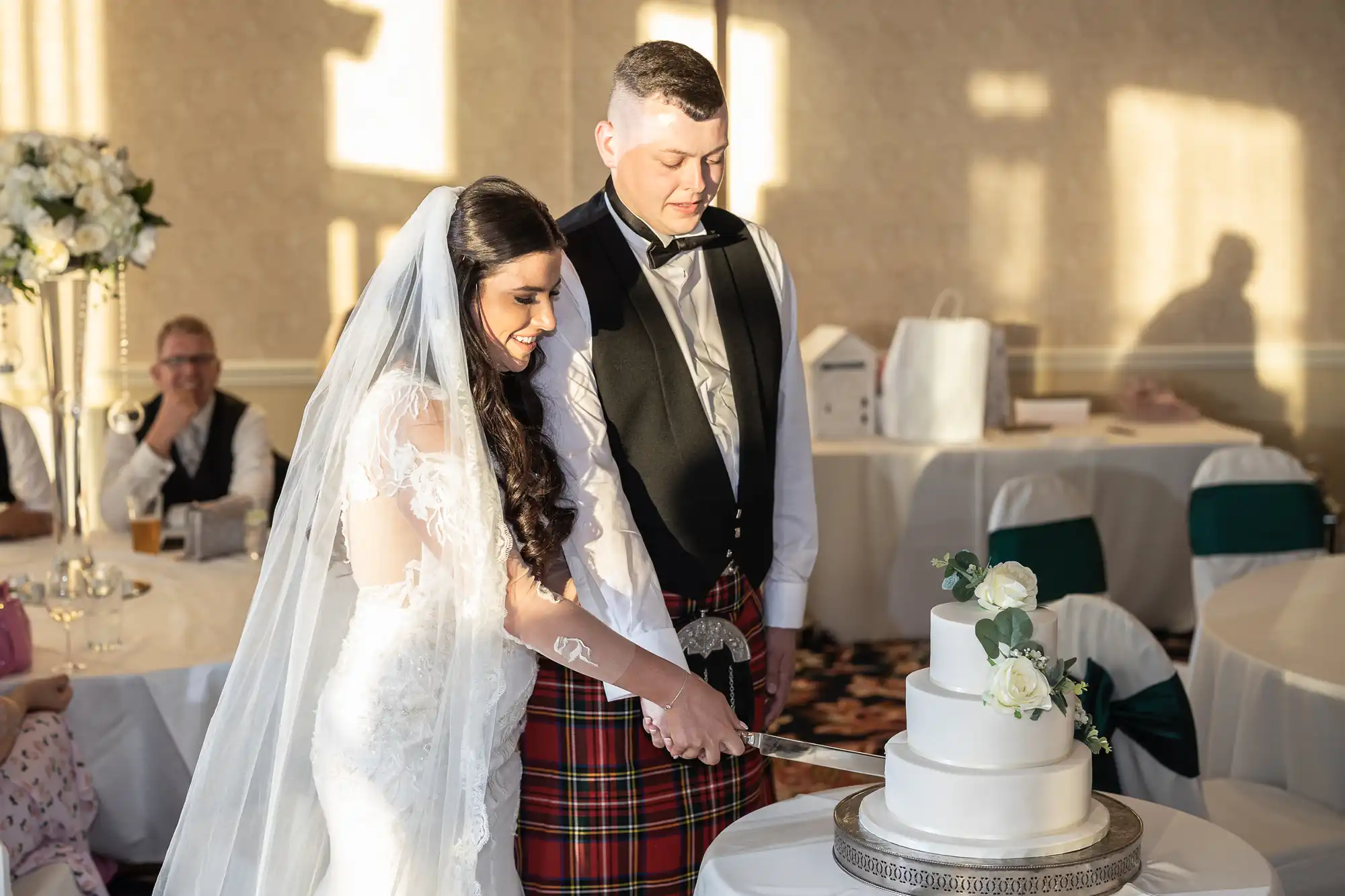 A bride and groom in wedding attire cutting a cake together at their reception.