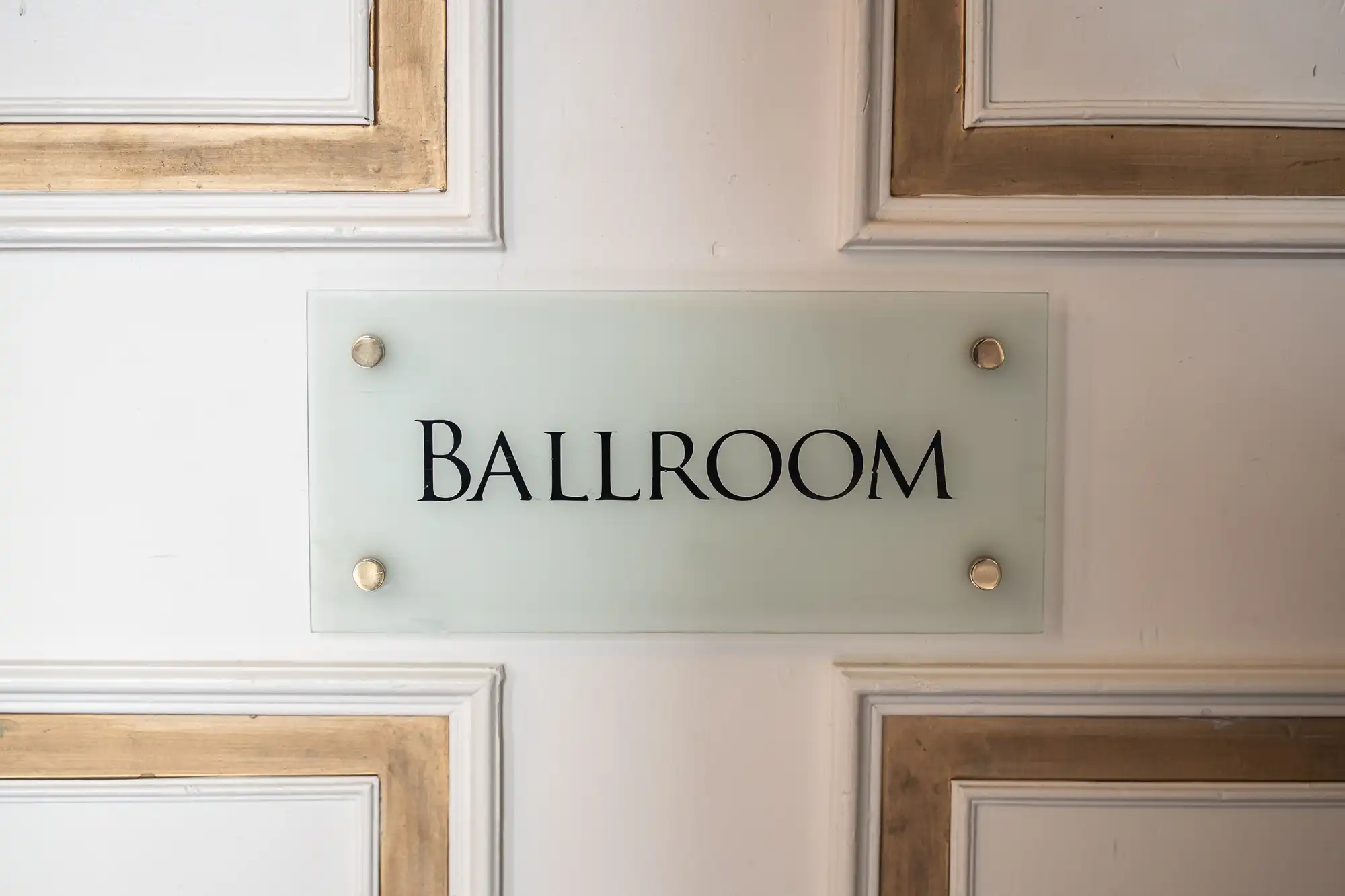 A white door with gold accents features a frosted glass sign reading "Ballroom.