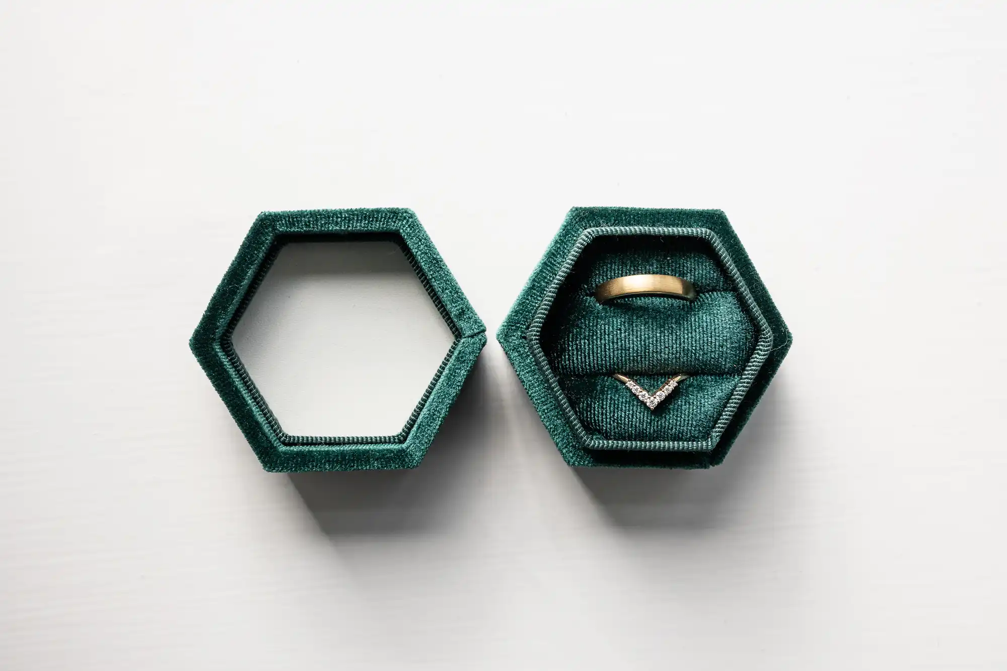 A teal hexagonal ring box is shown open. The left side is empty, and the right side holds a gold ring and a V-shaped diamond ring.