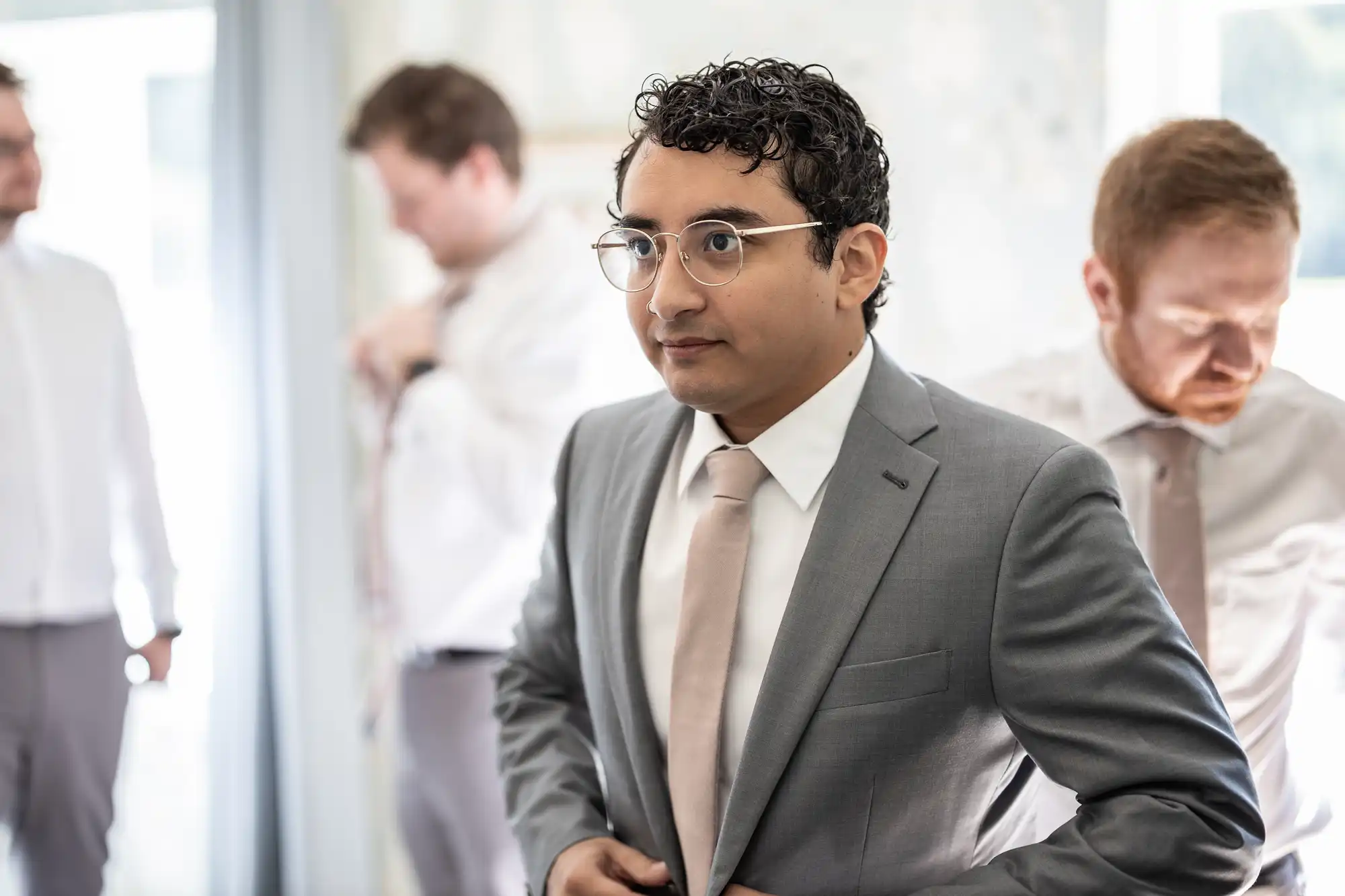 A person in a gray suit adjusts their jacket, with three other individuals in the background also preparing.