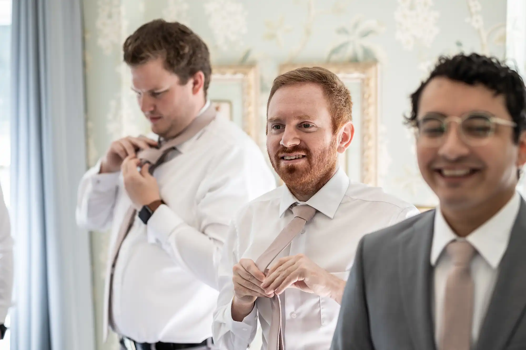 Three men in formal attire, with two adjusting their ties, and one smiling.