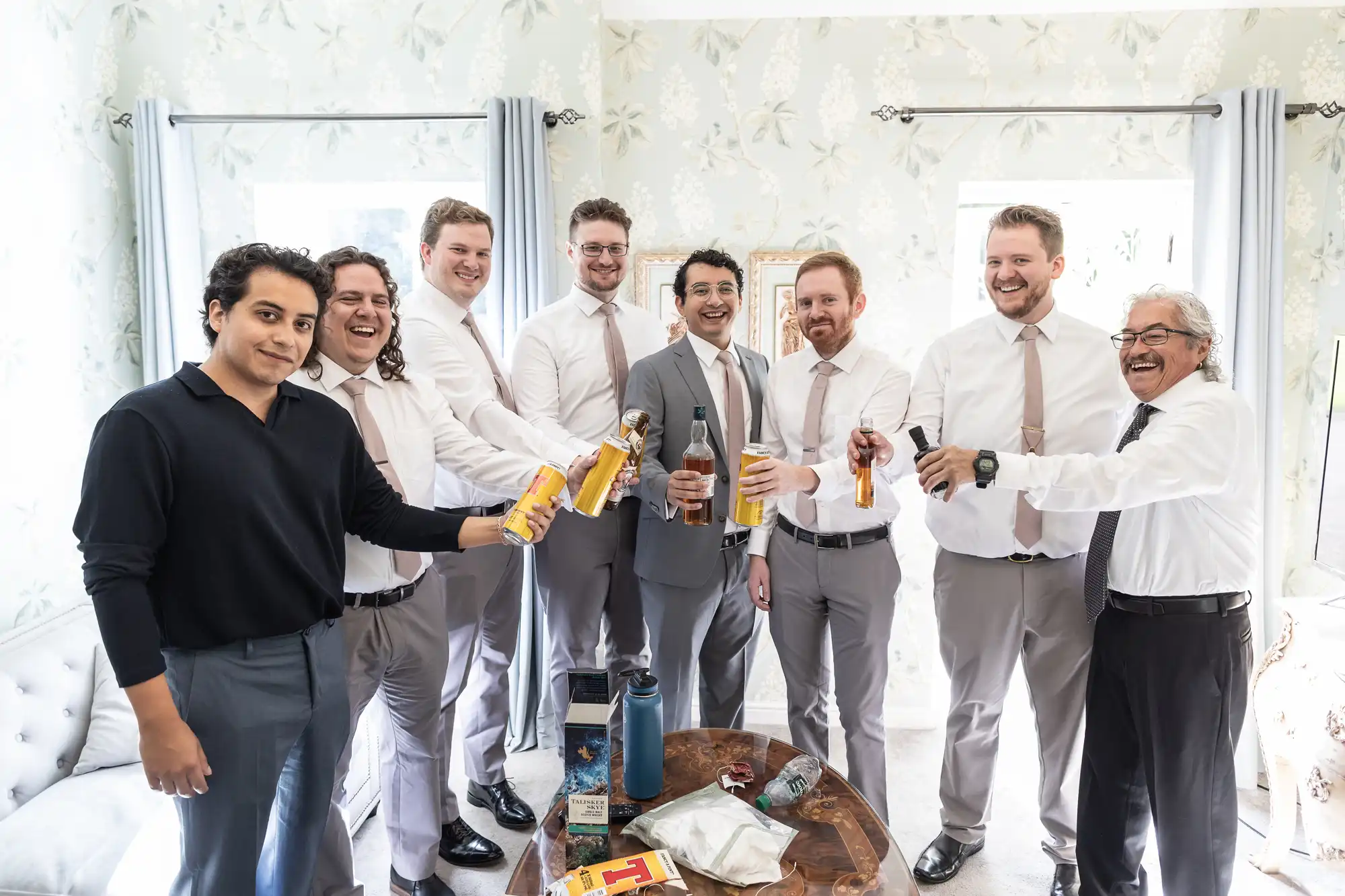 Eight men, dressed in formal and semi-formal attire, stand in a room holding beverages and smiling. They appear to be celebrating an event.