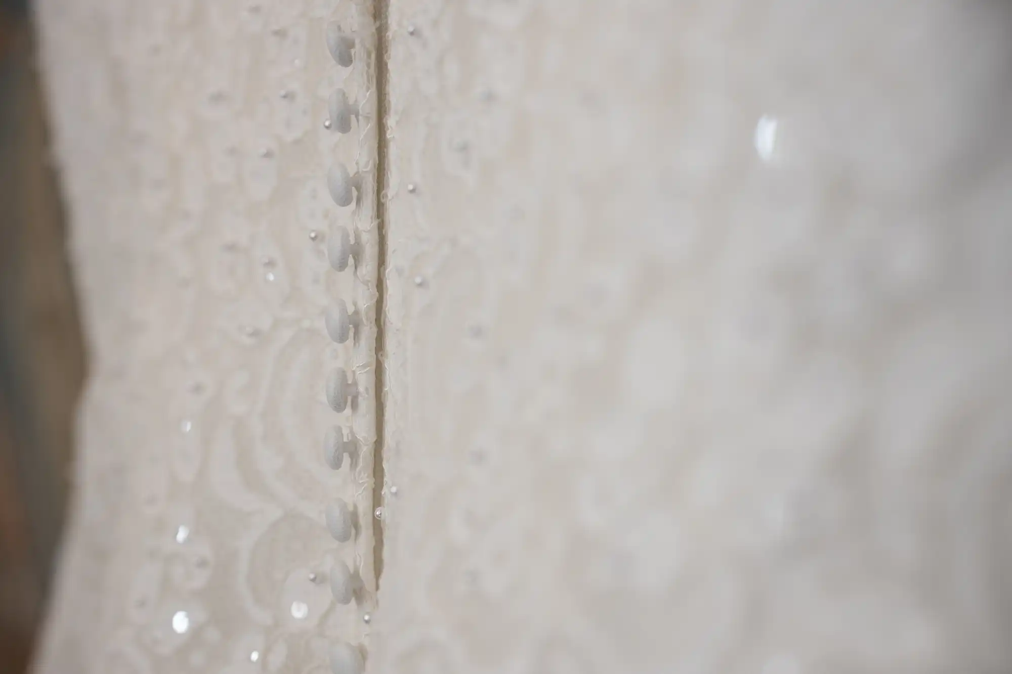 Close-up of a white wedding dress with intricate beadwork and lace detailing, showcasing a row of fabric-covered buttons.