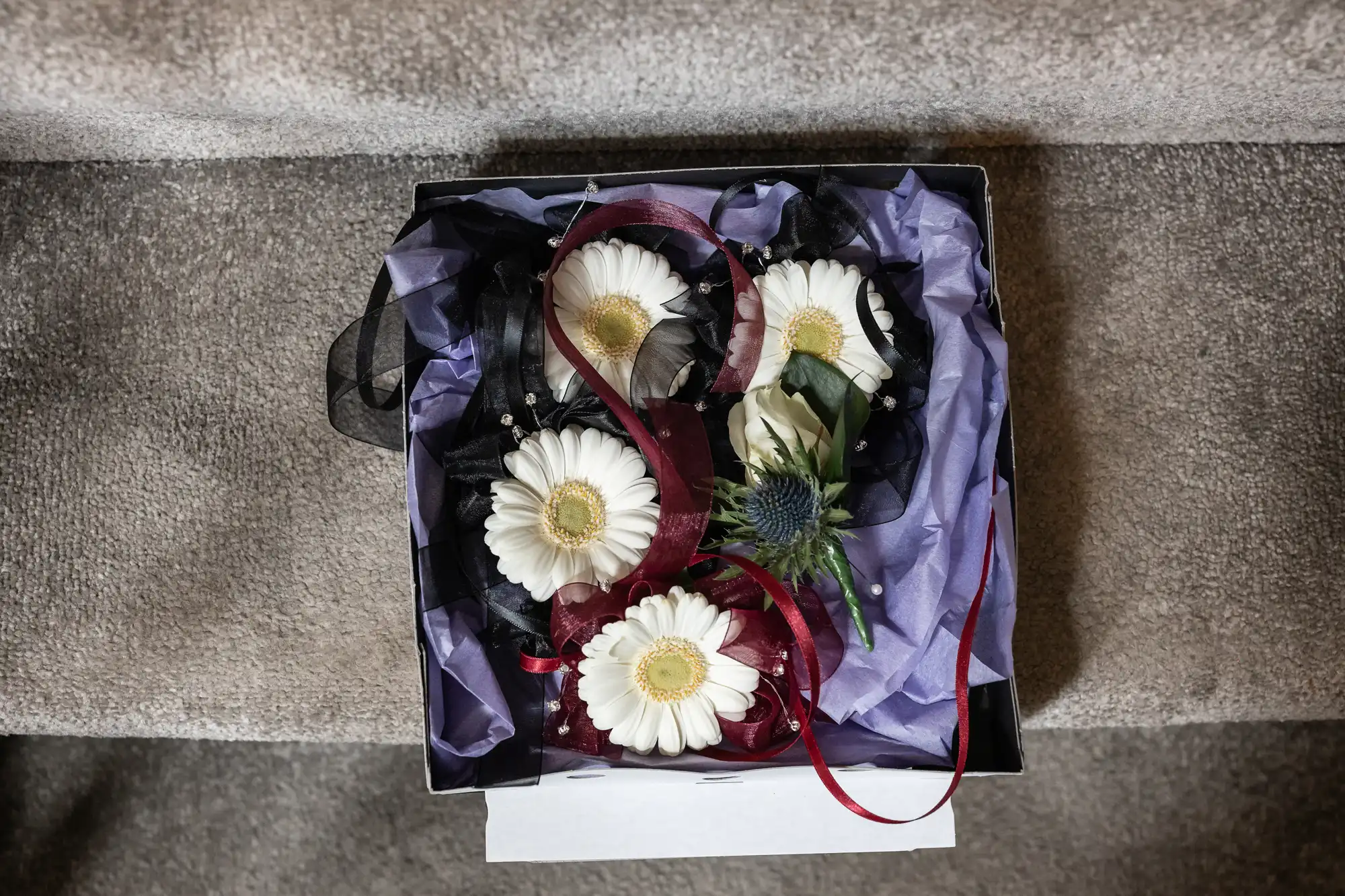 A box containing white flowers with black and red ribbon accents, placed on a carpeted staircase.