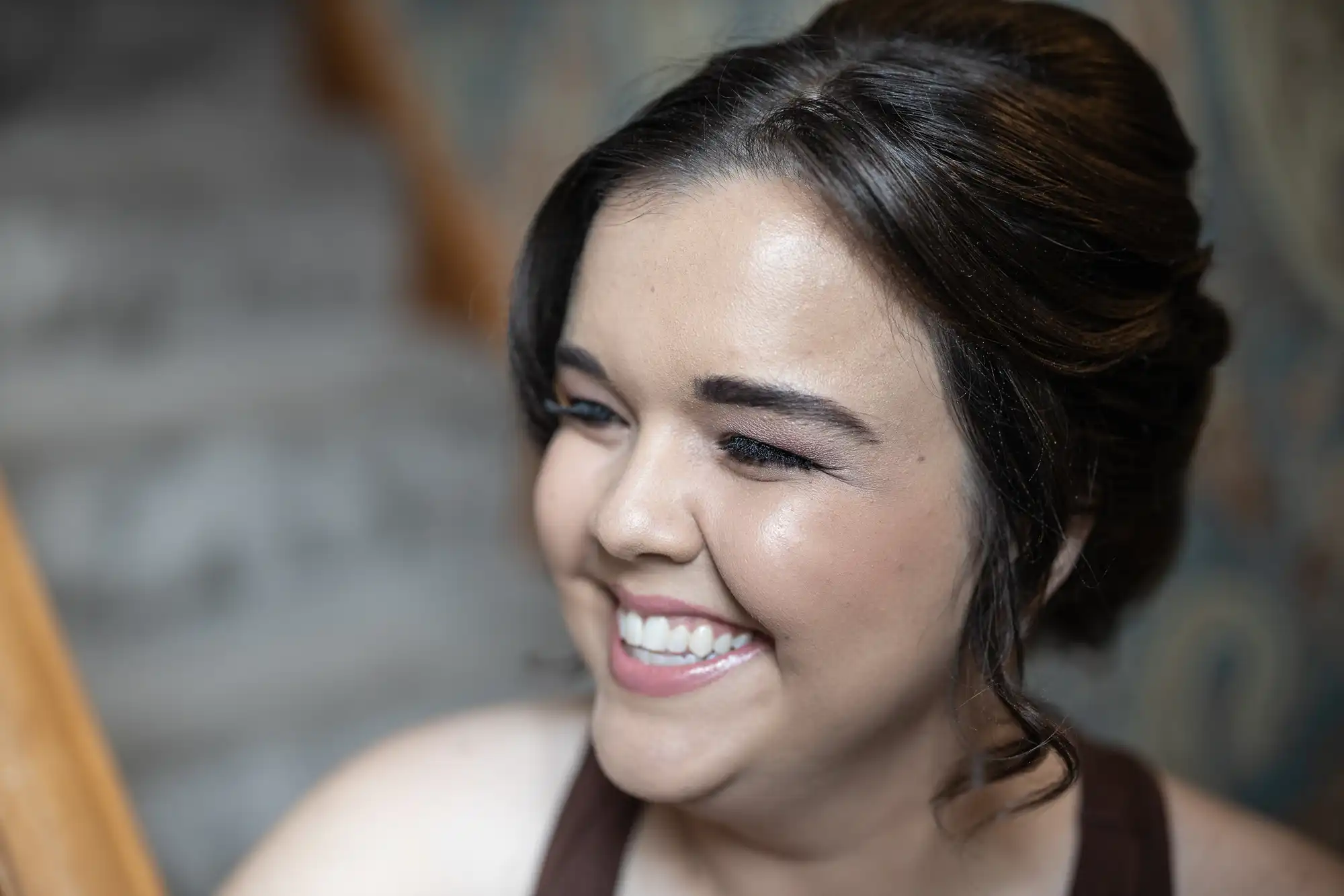 Woman smiling and looking to the side, with brunette hair styled in an updo, against a blurred background.